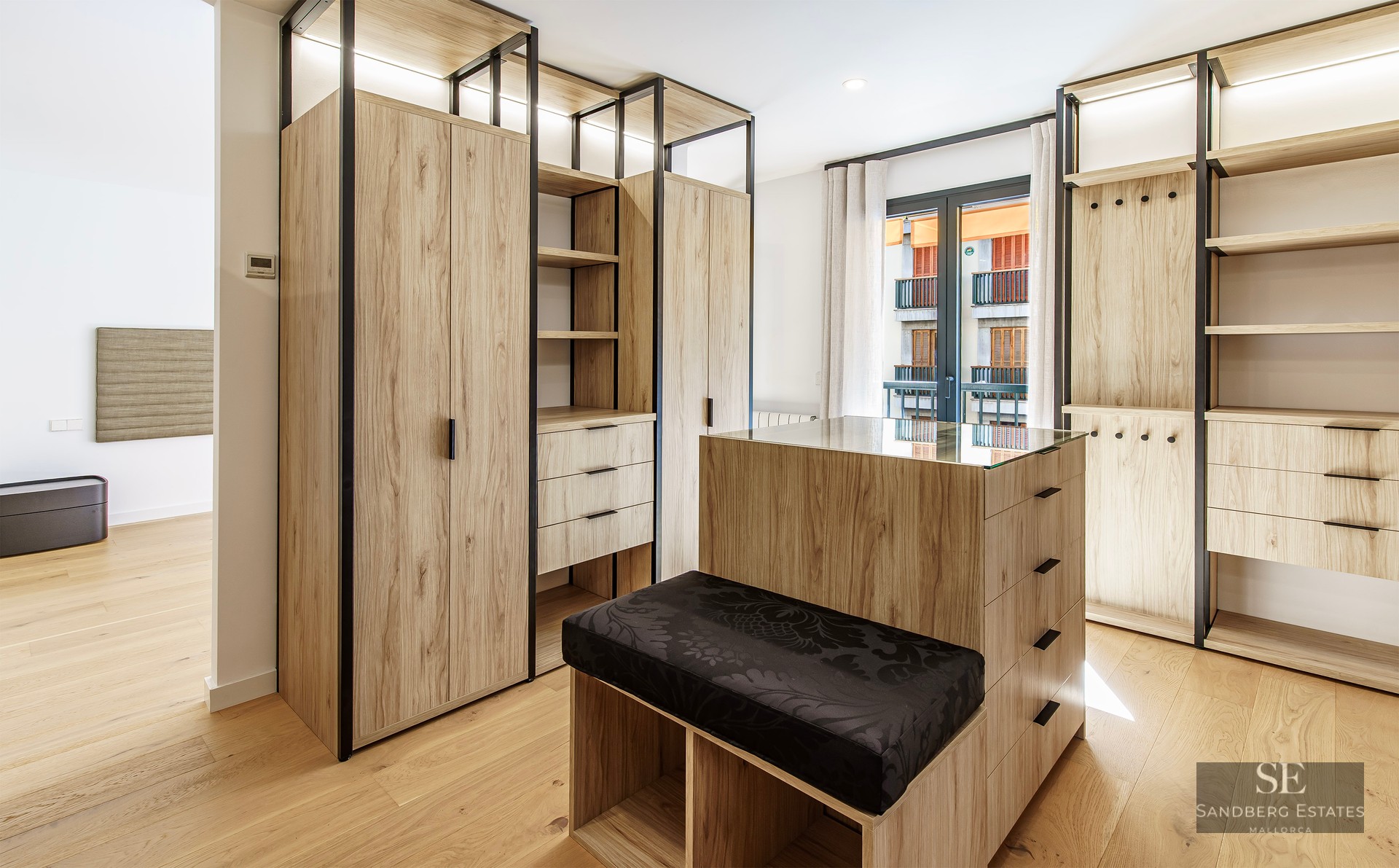 Grand dressing avec armoires en bois clair, îlot central avec plateau en verre et banc noir.