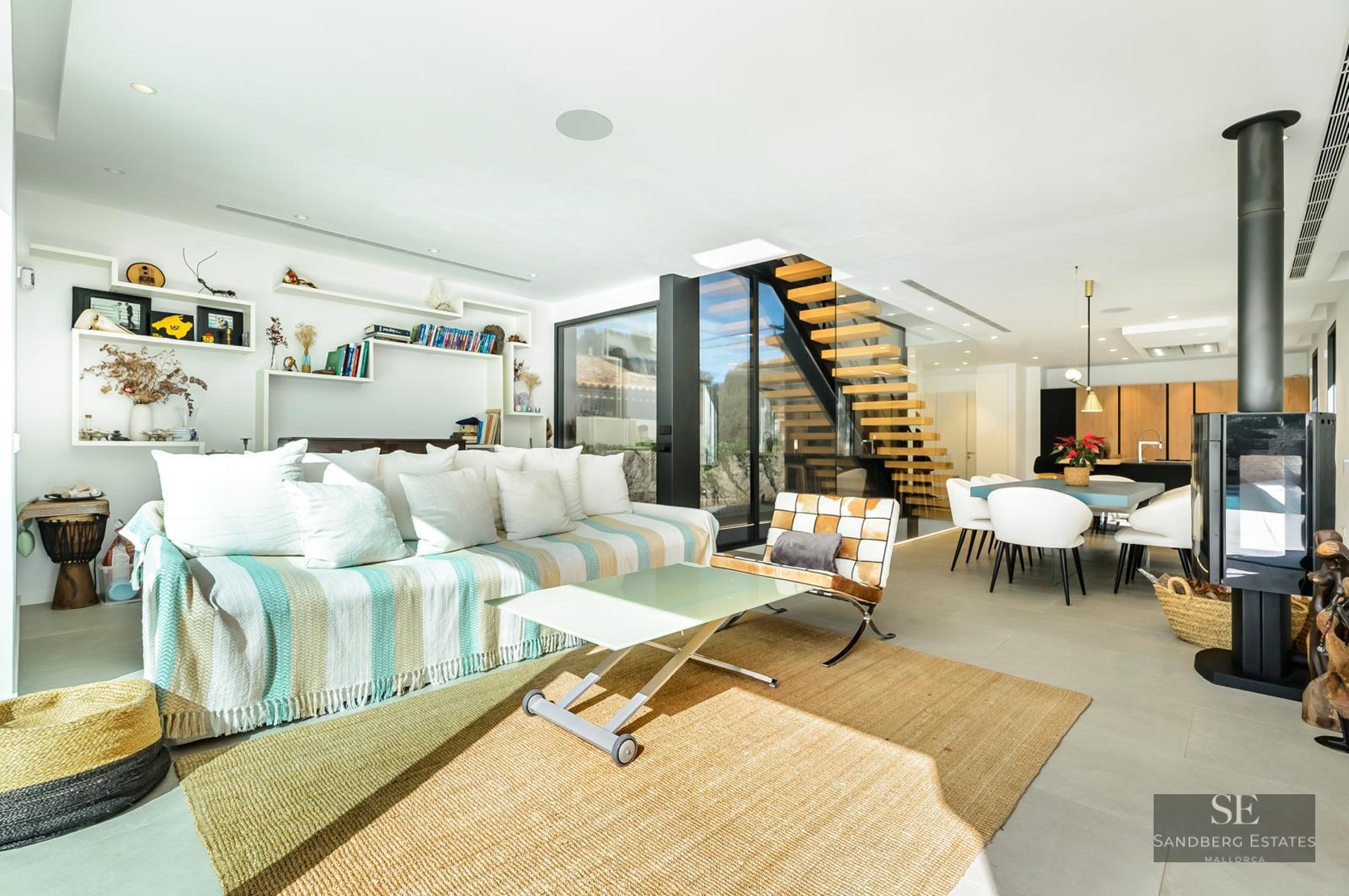 Bright modern living room with a striped sofa, floating wooden stairs, and a black freestanding fireplace.