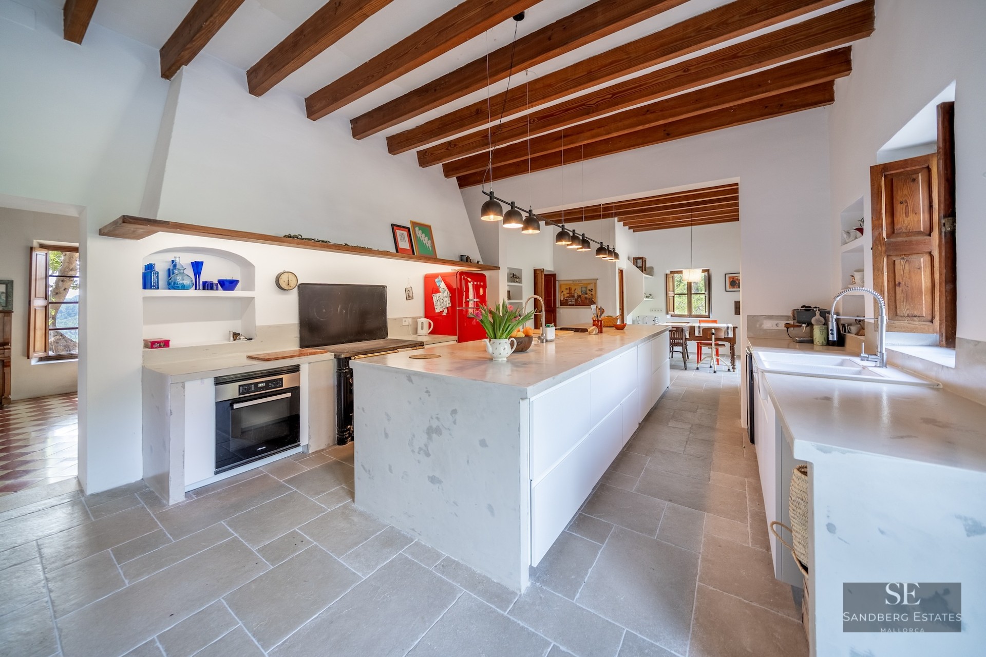 Spacious kitchen with exposed wood beams, a large white stone island, and a retro red refrigerator.