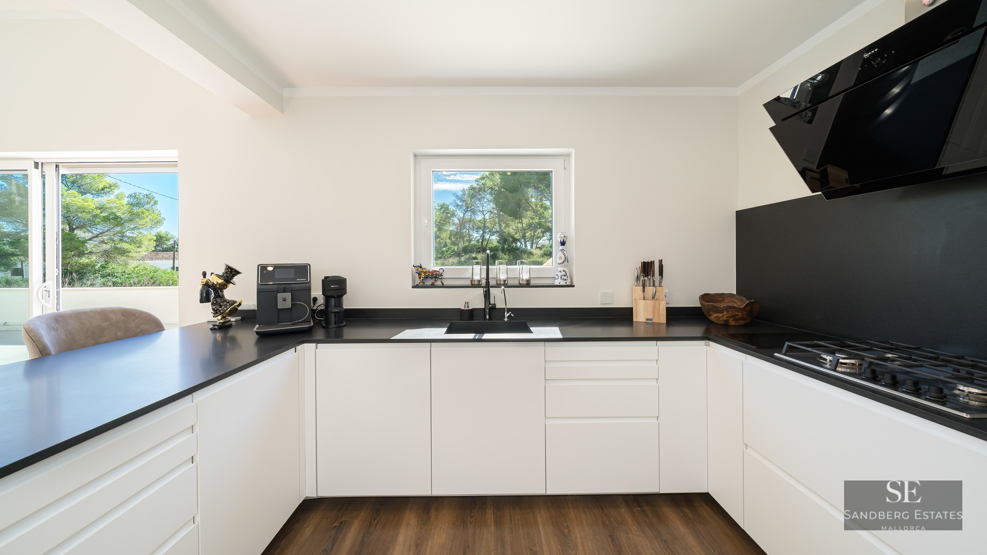 Cuisine moderne avec placards blancs, plans de travail noirs et une fenêtre donnant sur des arbres verts.