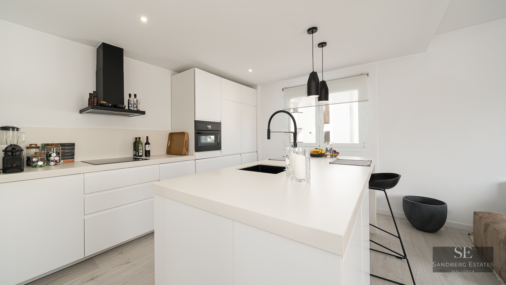 Modern white kitchen with a large island, black faucet, and sleek integrated appliances.
