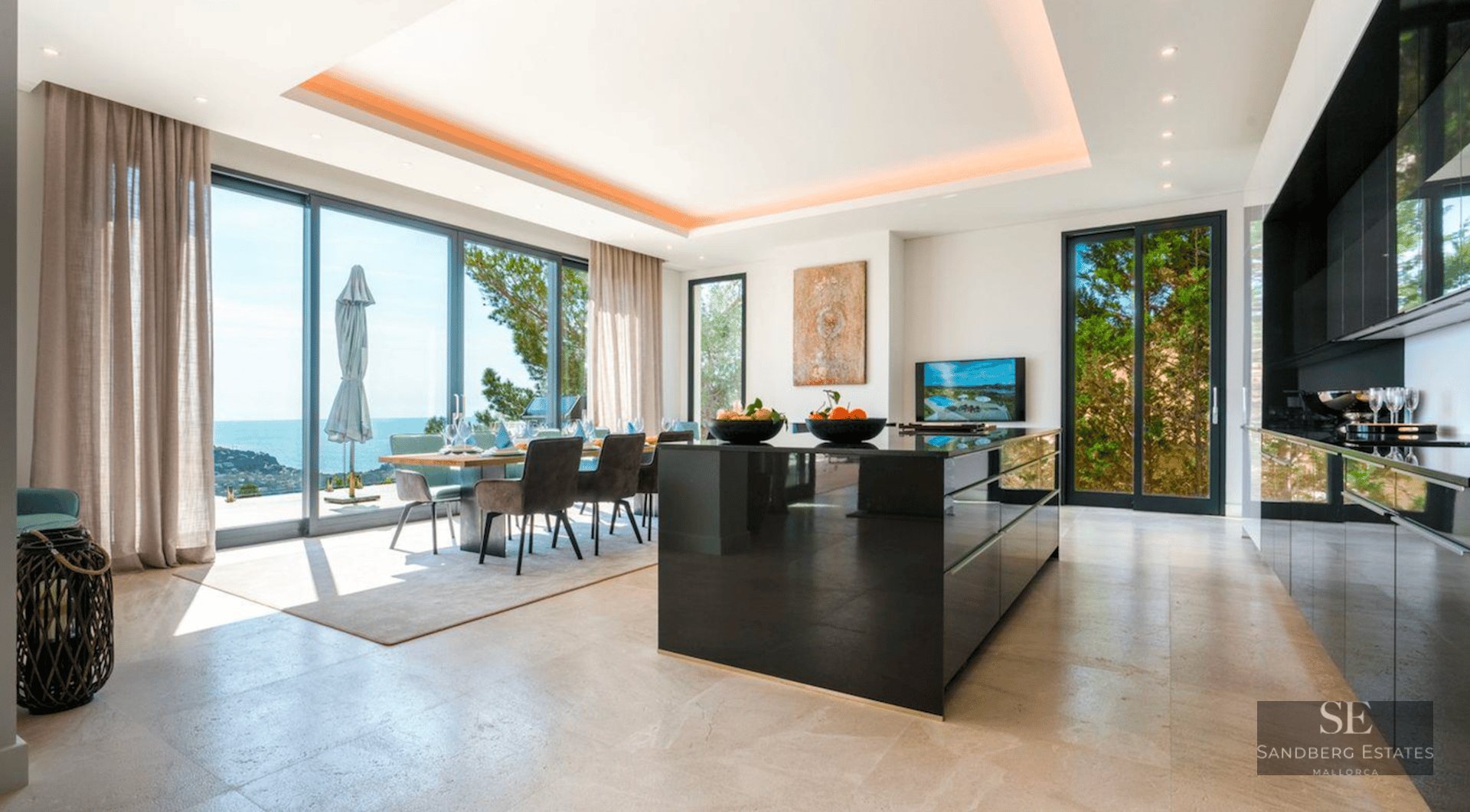 Modern kitchen and dining room with a black glossy island and large windows showing a bright sea view.