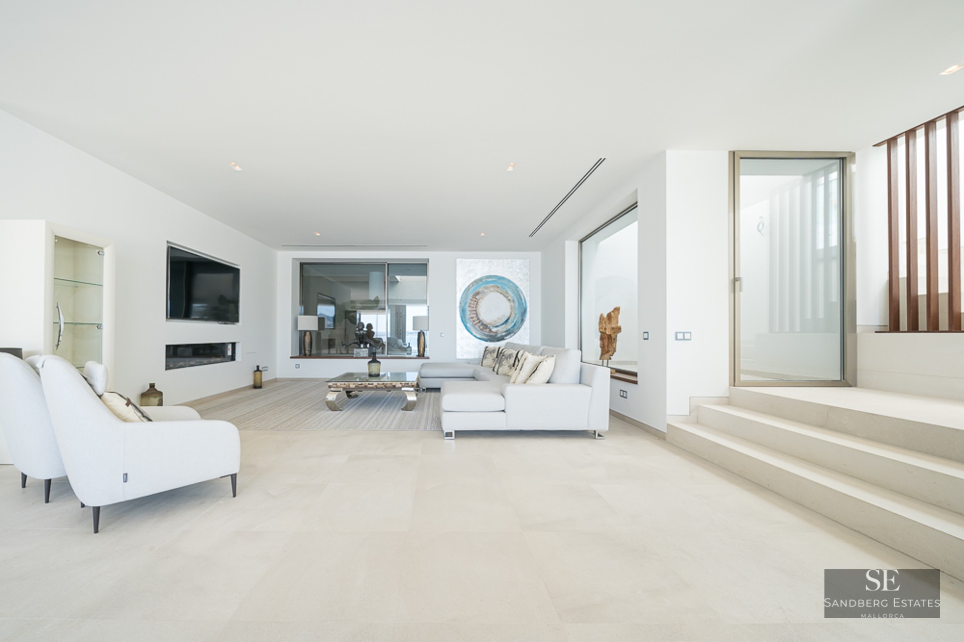 Bright minimalist living room with white sectional sofa, stone floors, linear fireplace, and modern art piece.