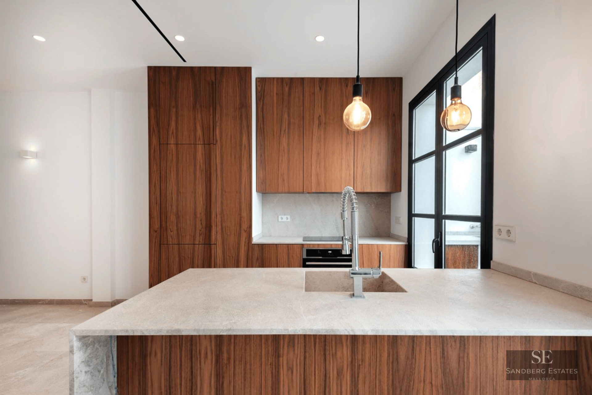 Modern kitchen featuring elegant walnut wood cabinetry, stone island with sink, and designer pendant lighting.