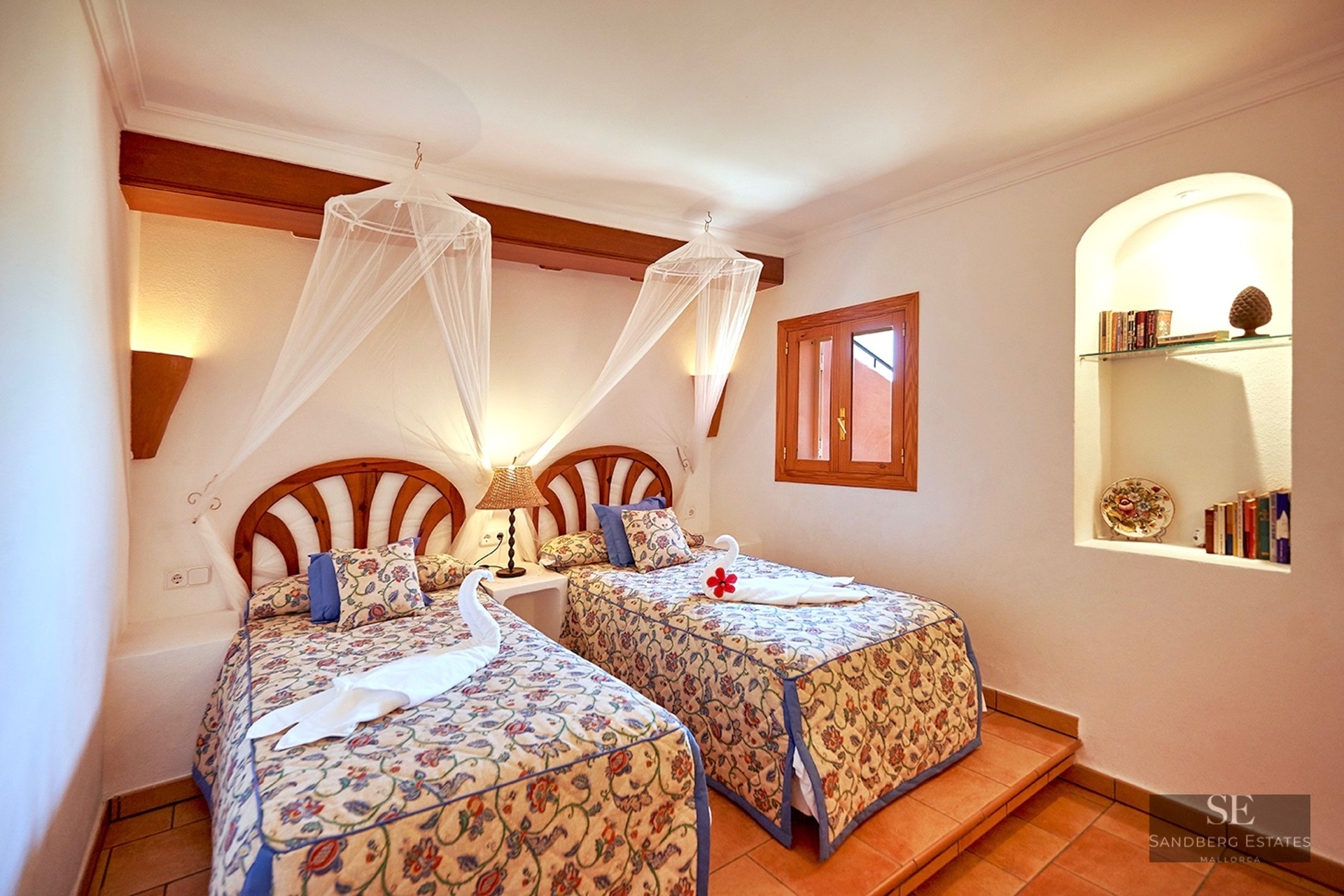 Two twin beds with floral covers and mosquito nets in a Mediterranean bedroom with terracotta floors.