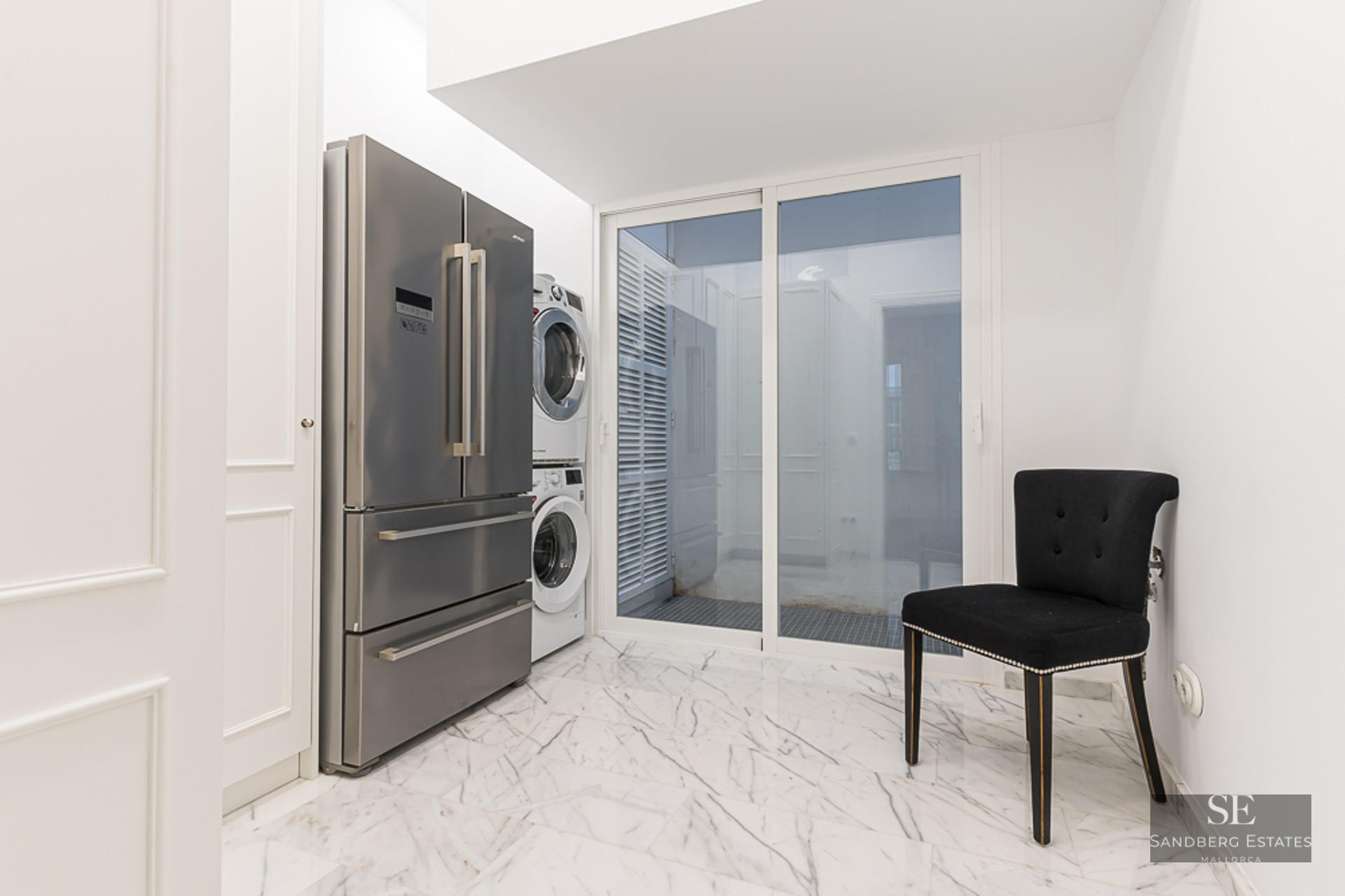 Utility room featuring a stainless steel refrigerator, stacked laundry unit, and white marble flooring.