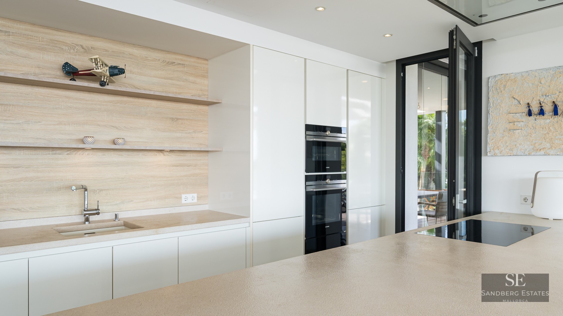 A modern kitchen featuring white cabinetry, wooden shelving, a stone island, and integrated high-end appliances.