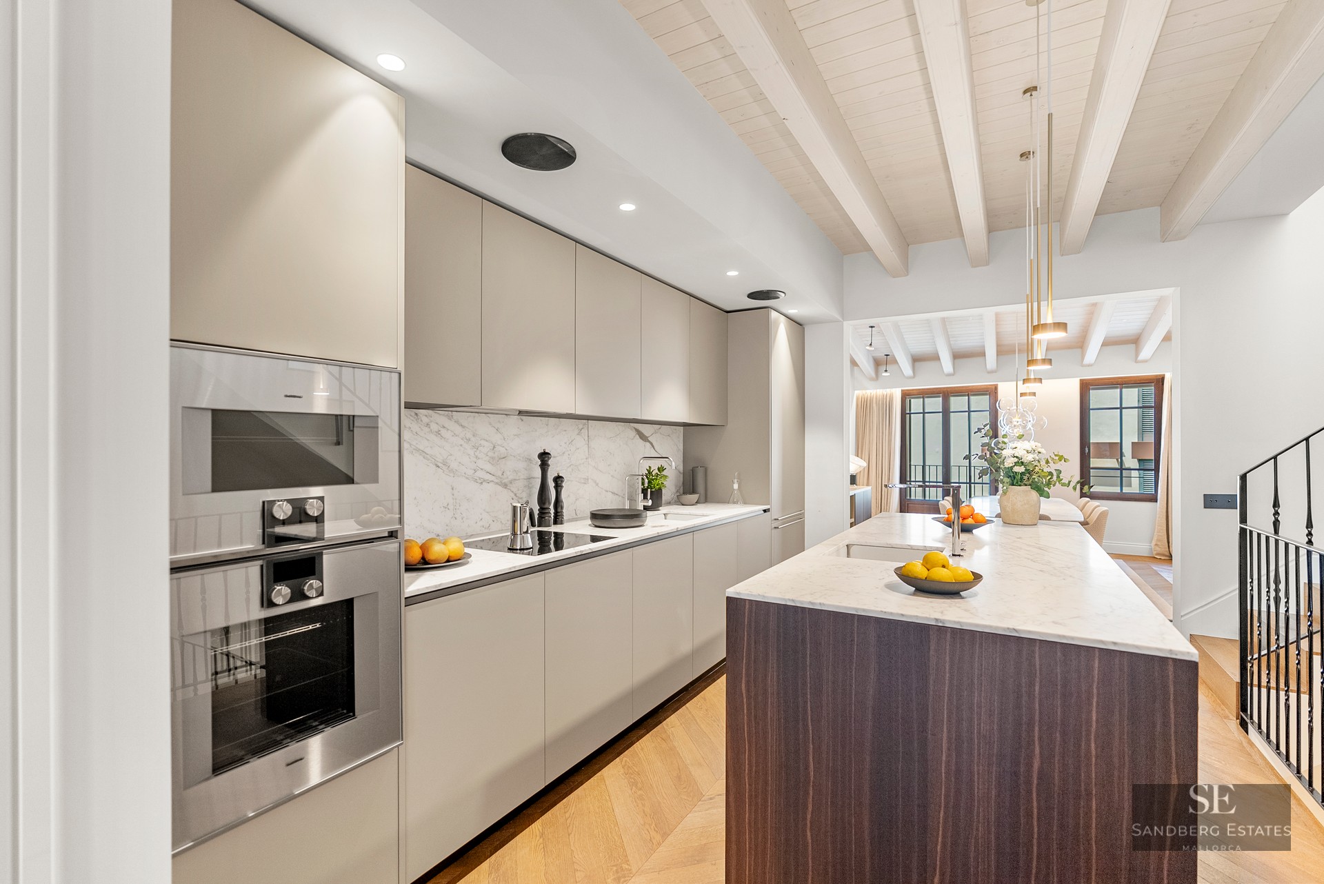 Modern kitchen with beige cabinets, white marble countertop, dark wood island, and light wood beamed ceiling.
