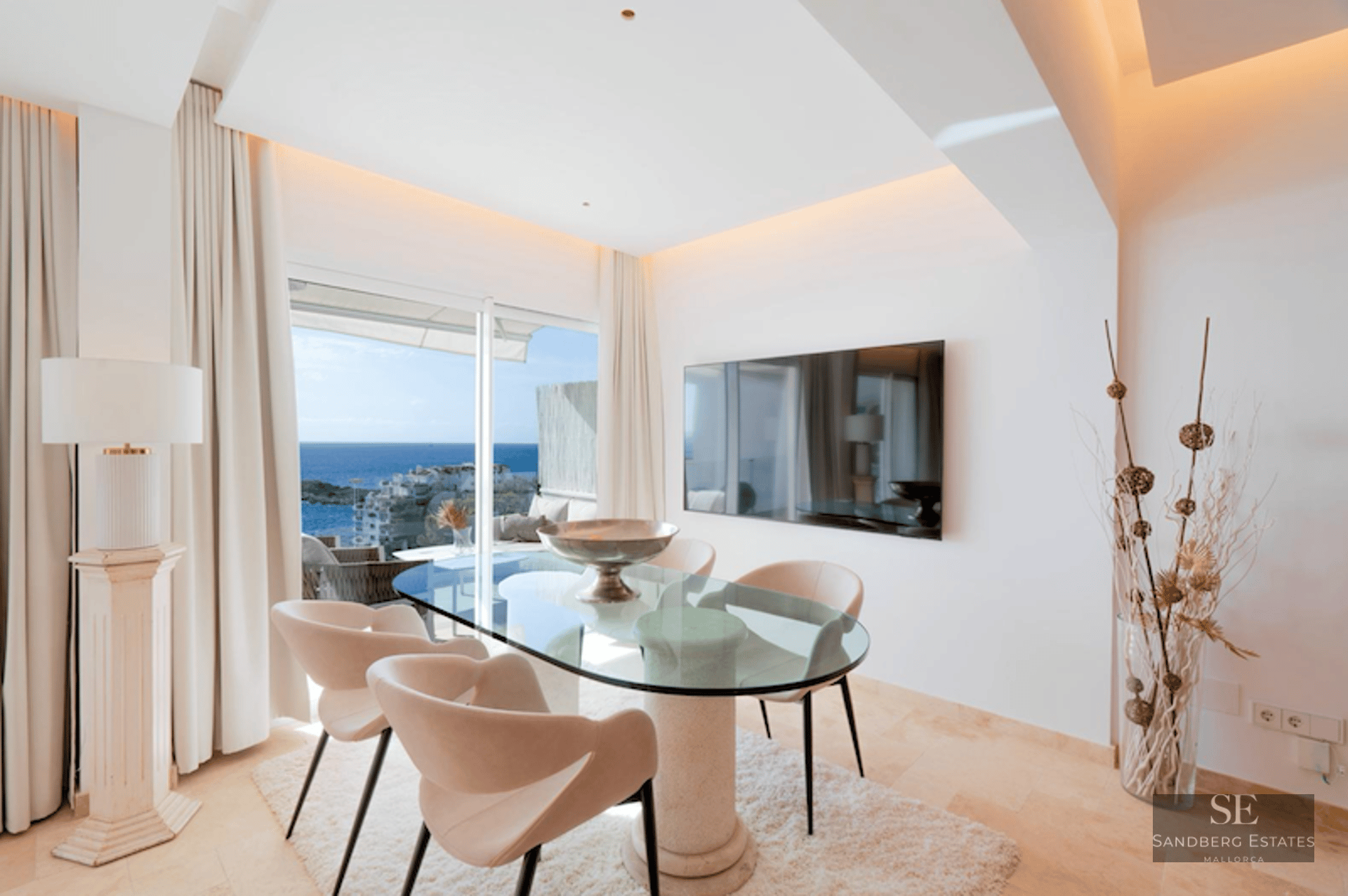 A modern dining room with a glass table, designer chairs, and large windows overlooking the Mediterranean sea.