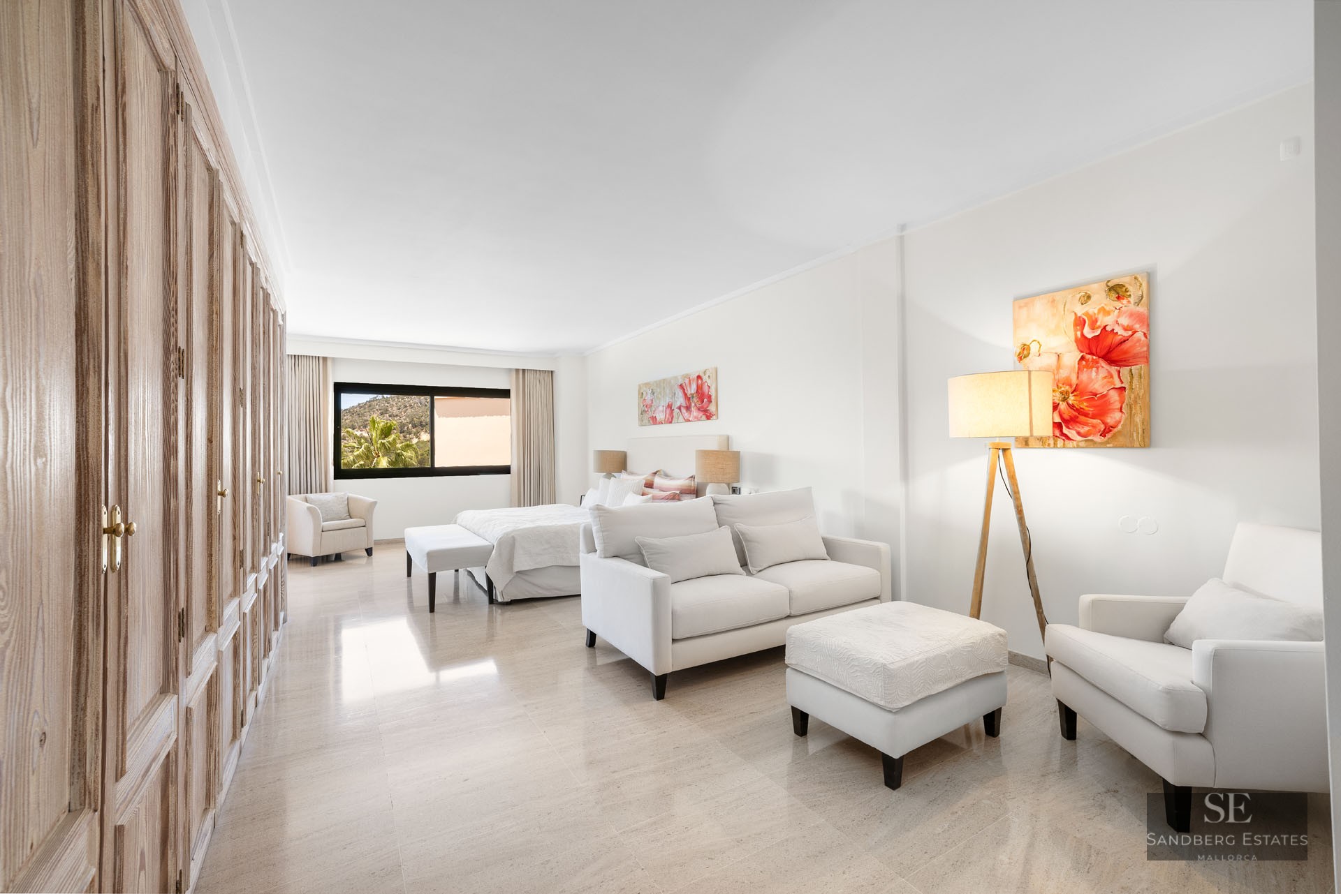 Suite lumineuse avec canapé blanc, armoires en bois, grand lit et art floral sur sol en marbre poli.