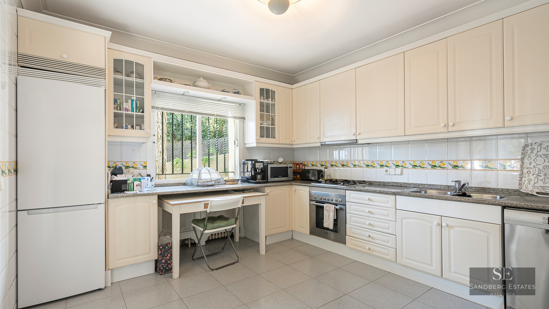 Spacious cream kitchen with granite counters, small dining table by a window, and integrated appliances.