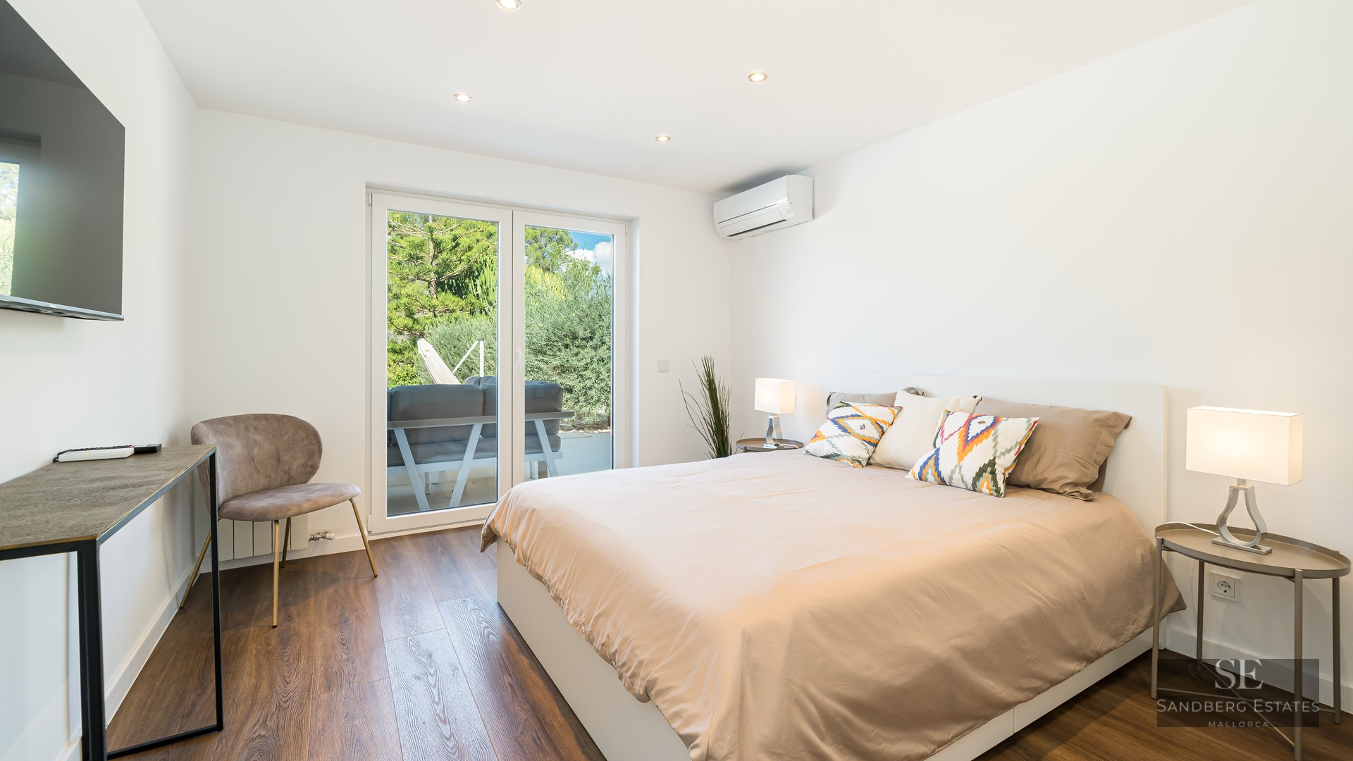 Chambre lumineuse avec grand lit, parquet en bois et portes vitrées coulissantes donnant sur un jardin.