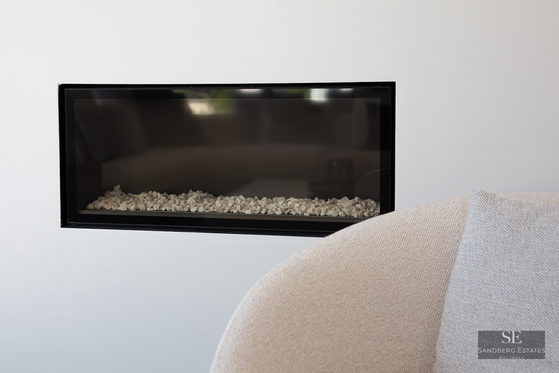 Close-up of a rectangular black-framed fireplace built into a white wall with white stones inside.