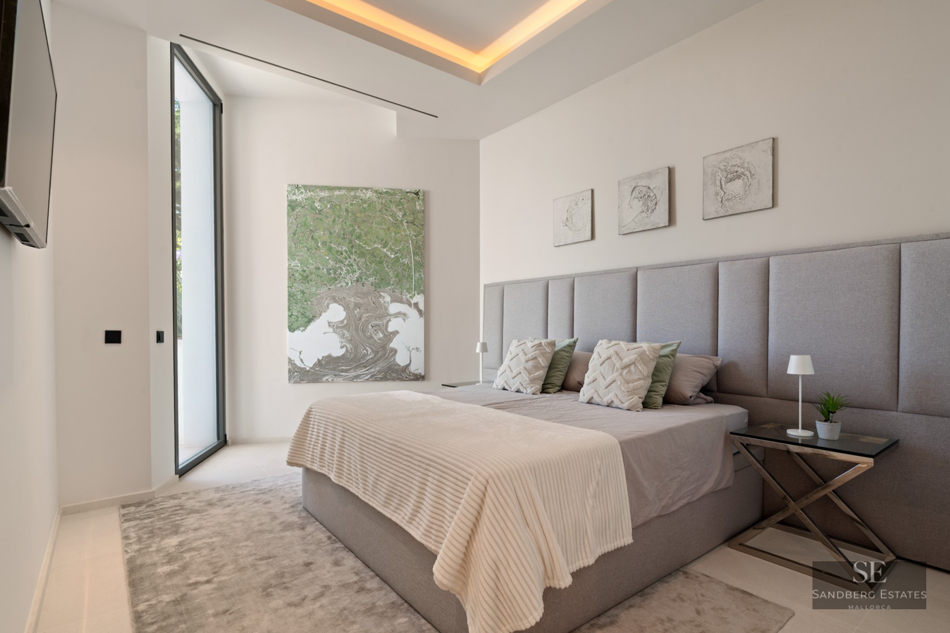 Bedroom with grey upholstered headboard, king-size bed, abstract art, and warm recessed lighting.