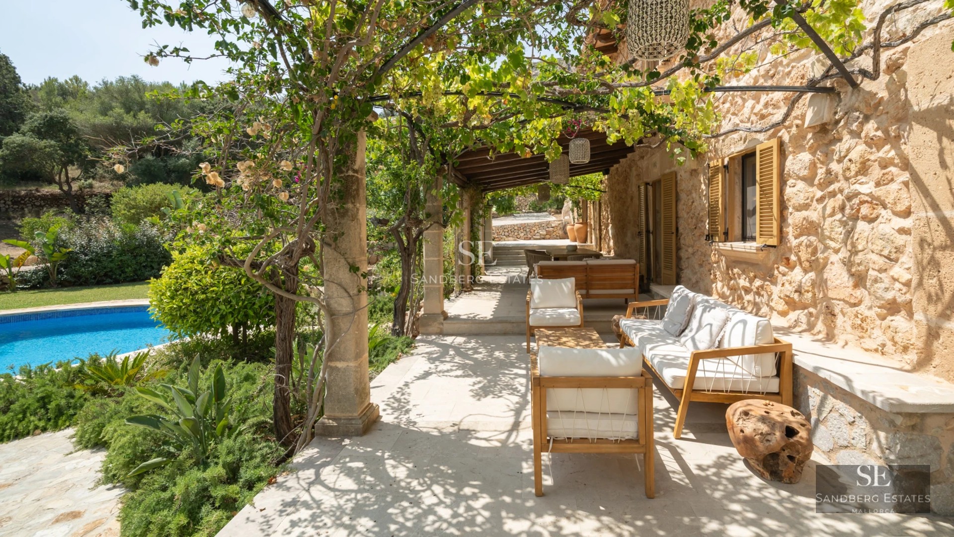 Large infinity pool bordered by a wooden deck and lush gardens. Modern facade with large windows.