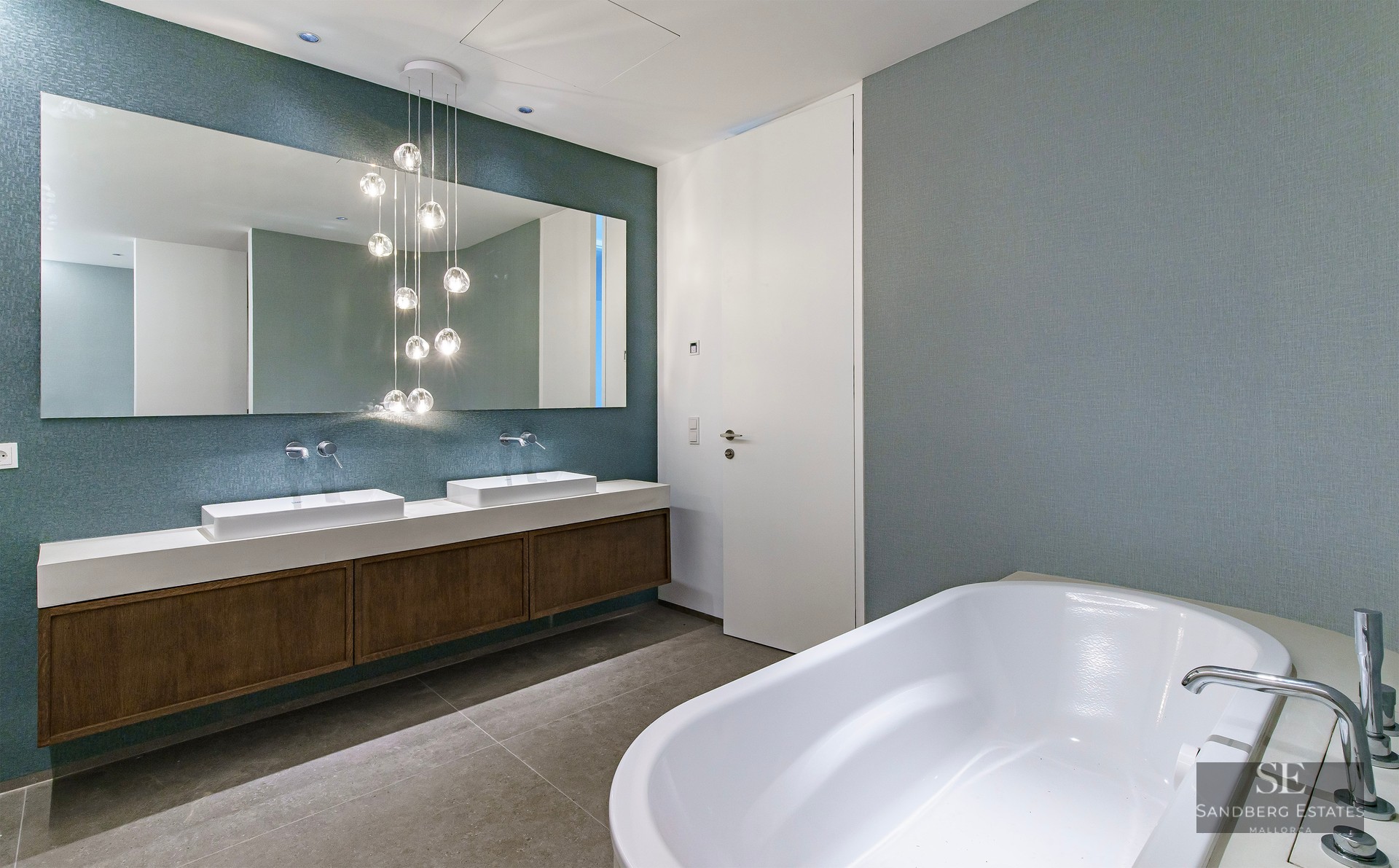 Luxury bathroom featuring a white bathtub, double vanity with wooden cabinets, and hanging glass globe lights.
