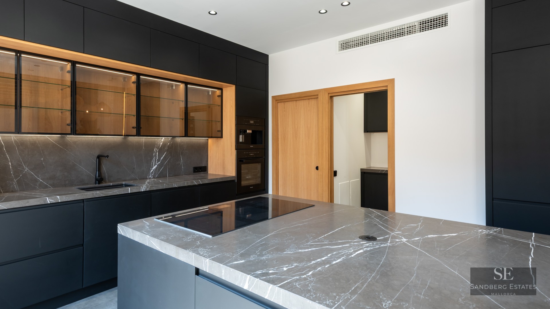 Modern kitchen featuring matte black cabinets, grey marble countertops, and warm wood accents.