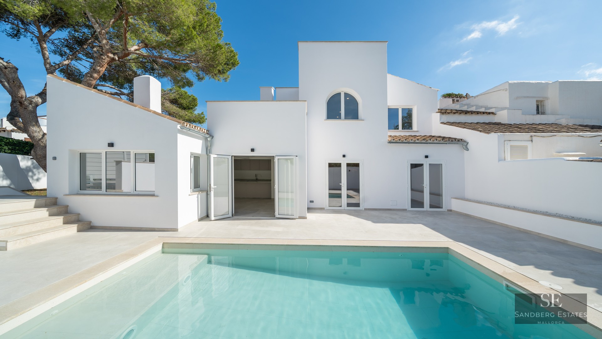 Turquoise swimming pool in front of a clean white modern Mediterranean villa under a clear blue sky.