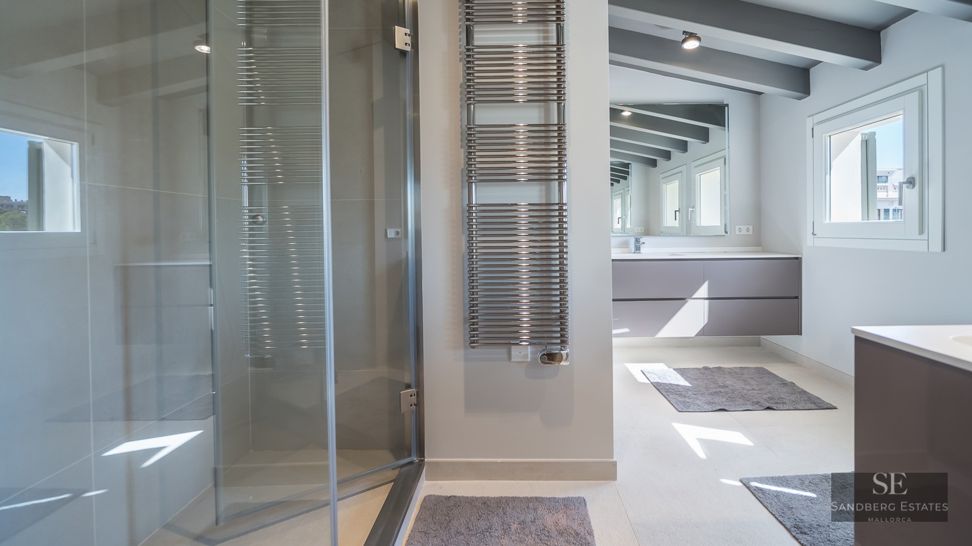 A contemporary bathroom featuring a glass-enclosed shower, chrome towel warmer, and grey ceiling beams.