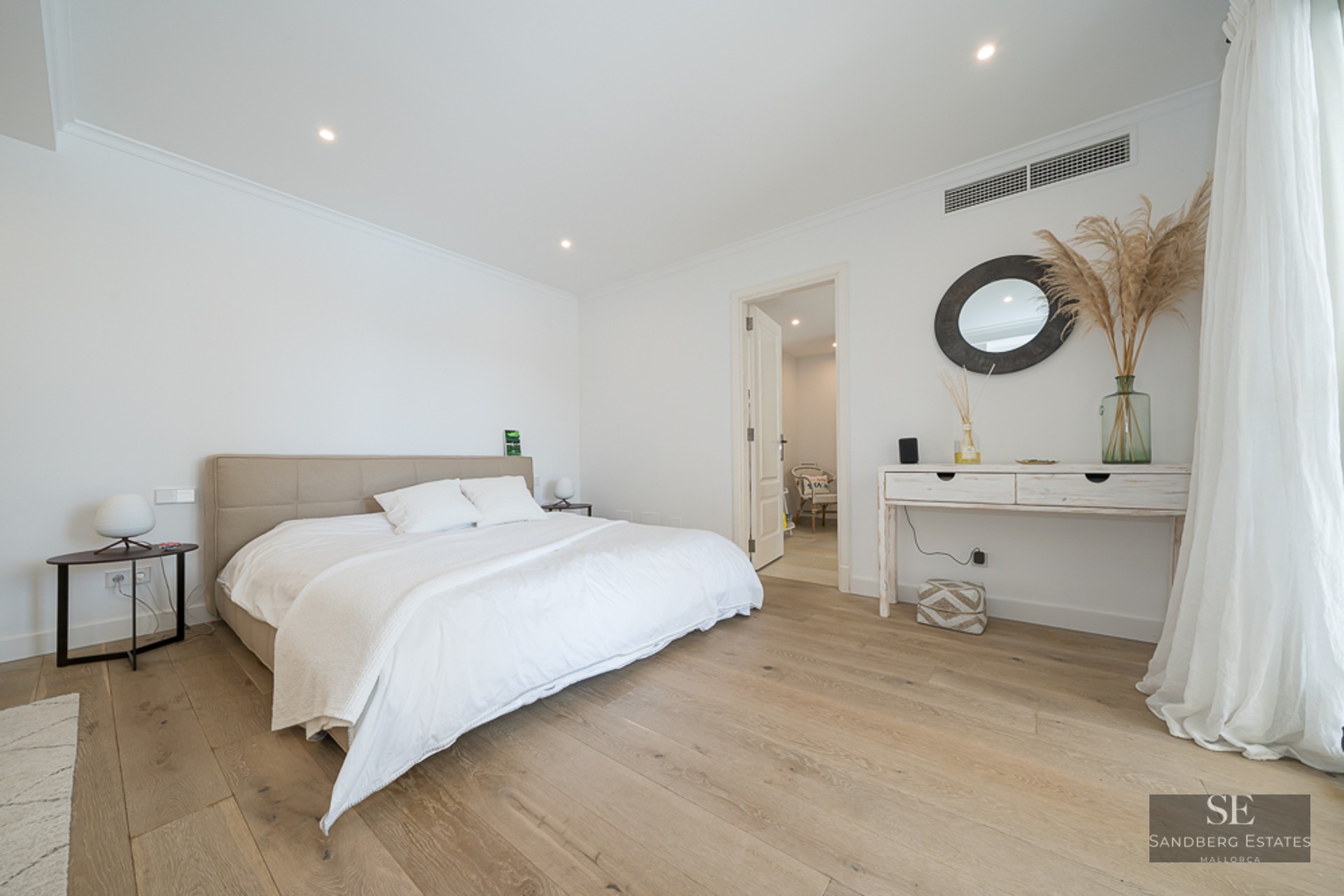 Chambre principale lumineuse avec lit blanc, parquet clair et console minimaliste avec miroir rond.