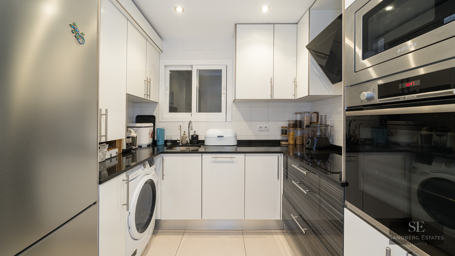 Cuisine moderne en U avec placards blancs, plans de travail noirs et appareils en acier inoxydable.