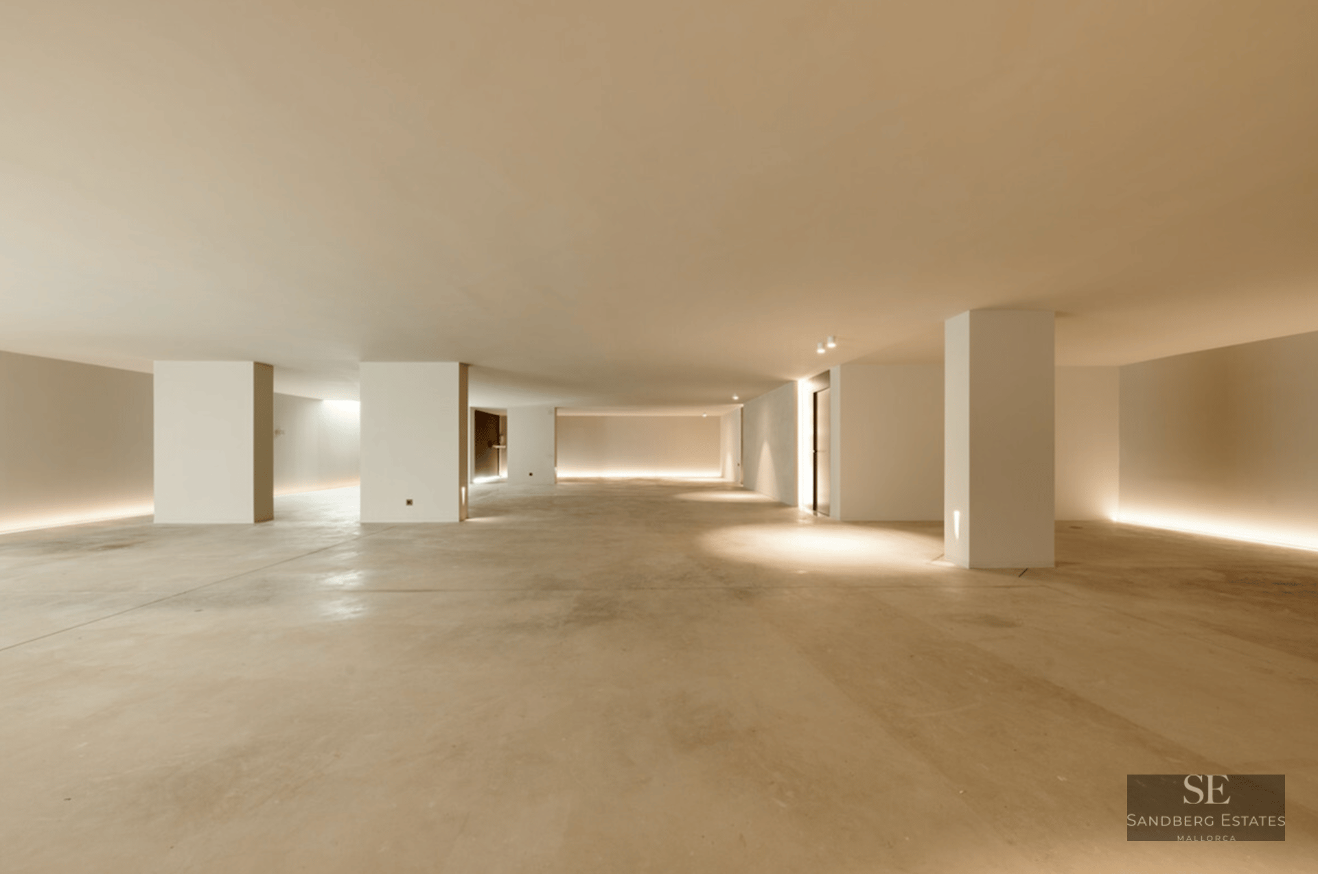Large minimalist interior space with polished concrete floors, white pillars, and indirect LED floor lighting.