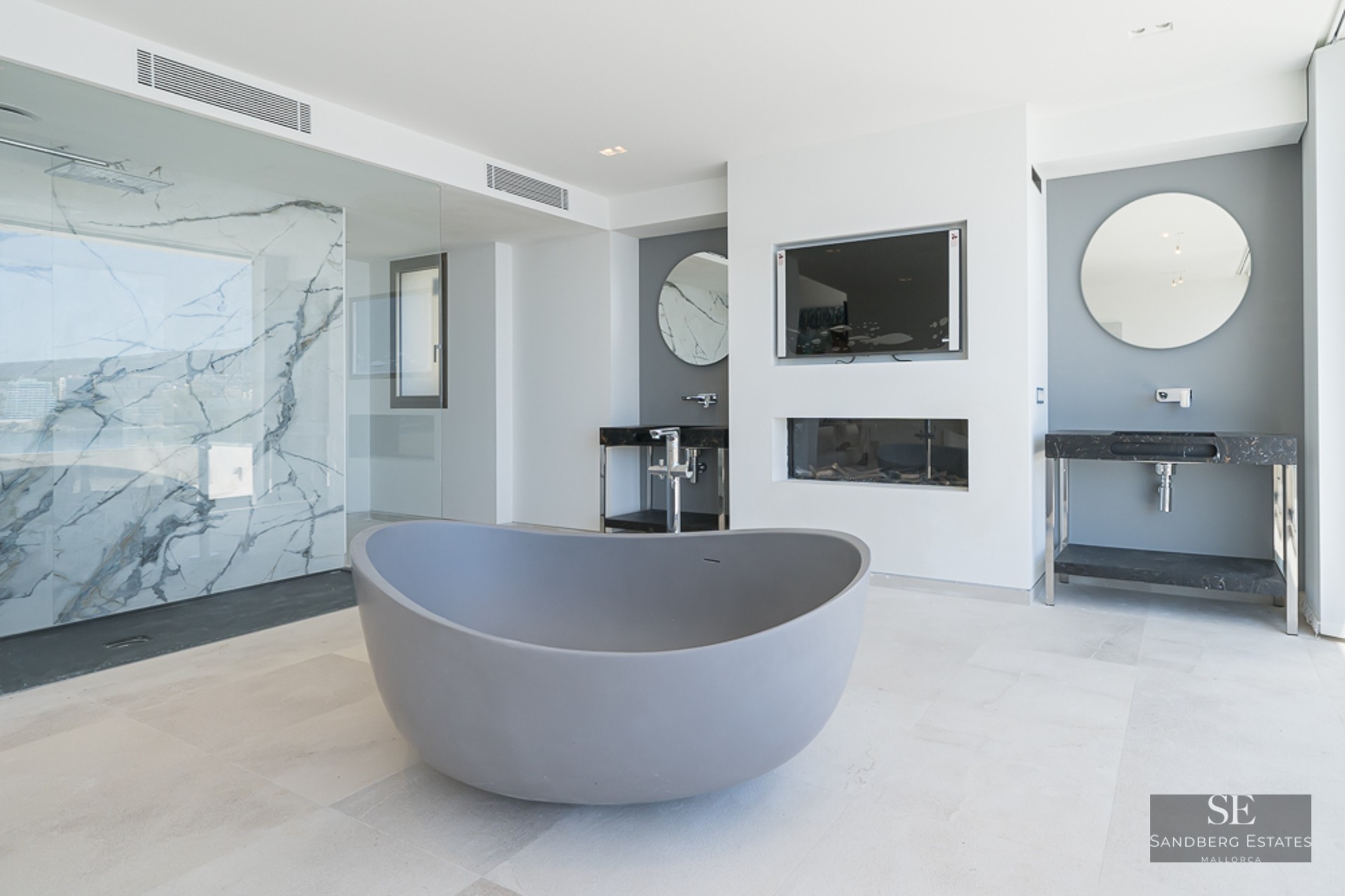 Modern bathroom featuring a grey freestanding tub, marble-walled shower, and dual vanities with round mirrors.