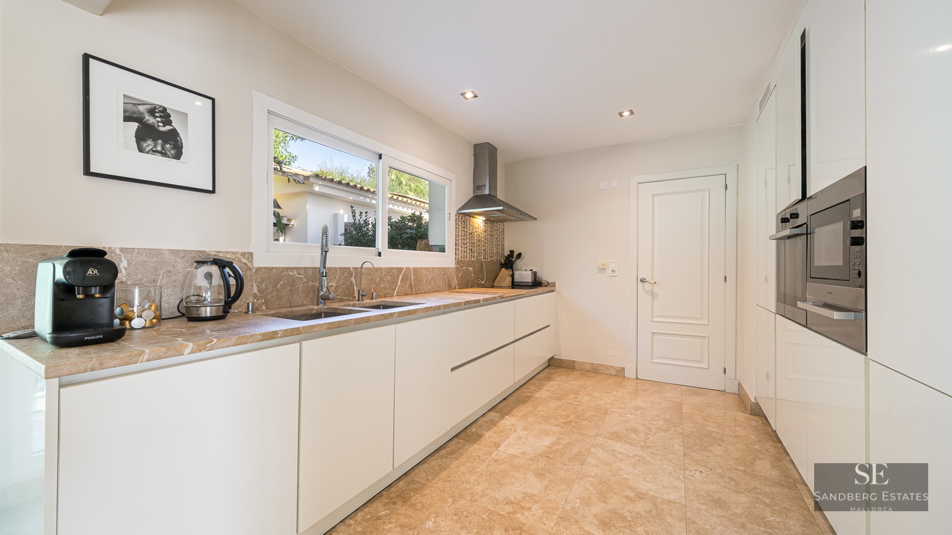 Modern kitchen with white cabinets, marble counters, stainless steel appliances, and a window viewing the outdoors.