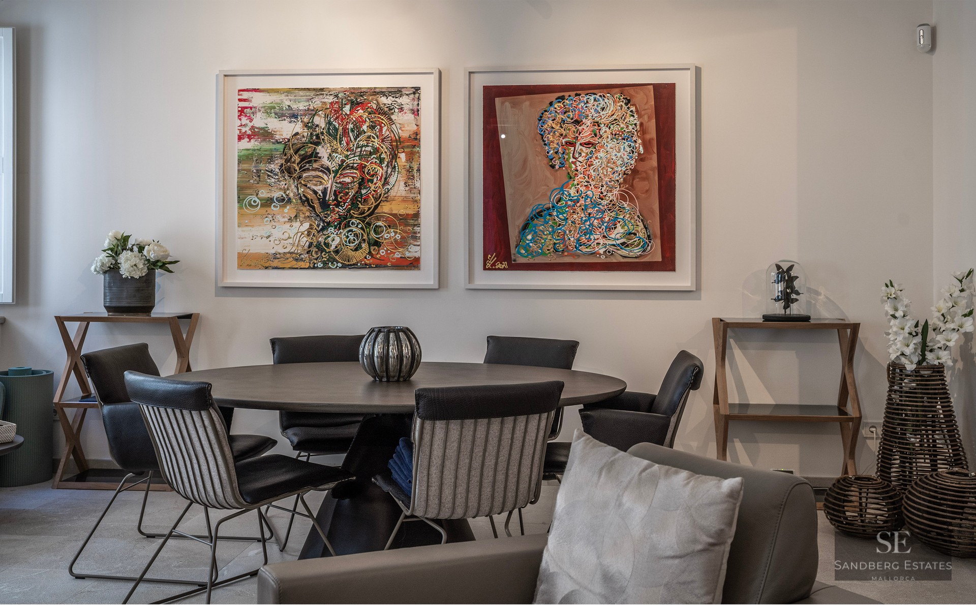Modern dining room featuring a dark round table, designer chairs, and two large abstract paintings on a white wall.