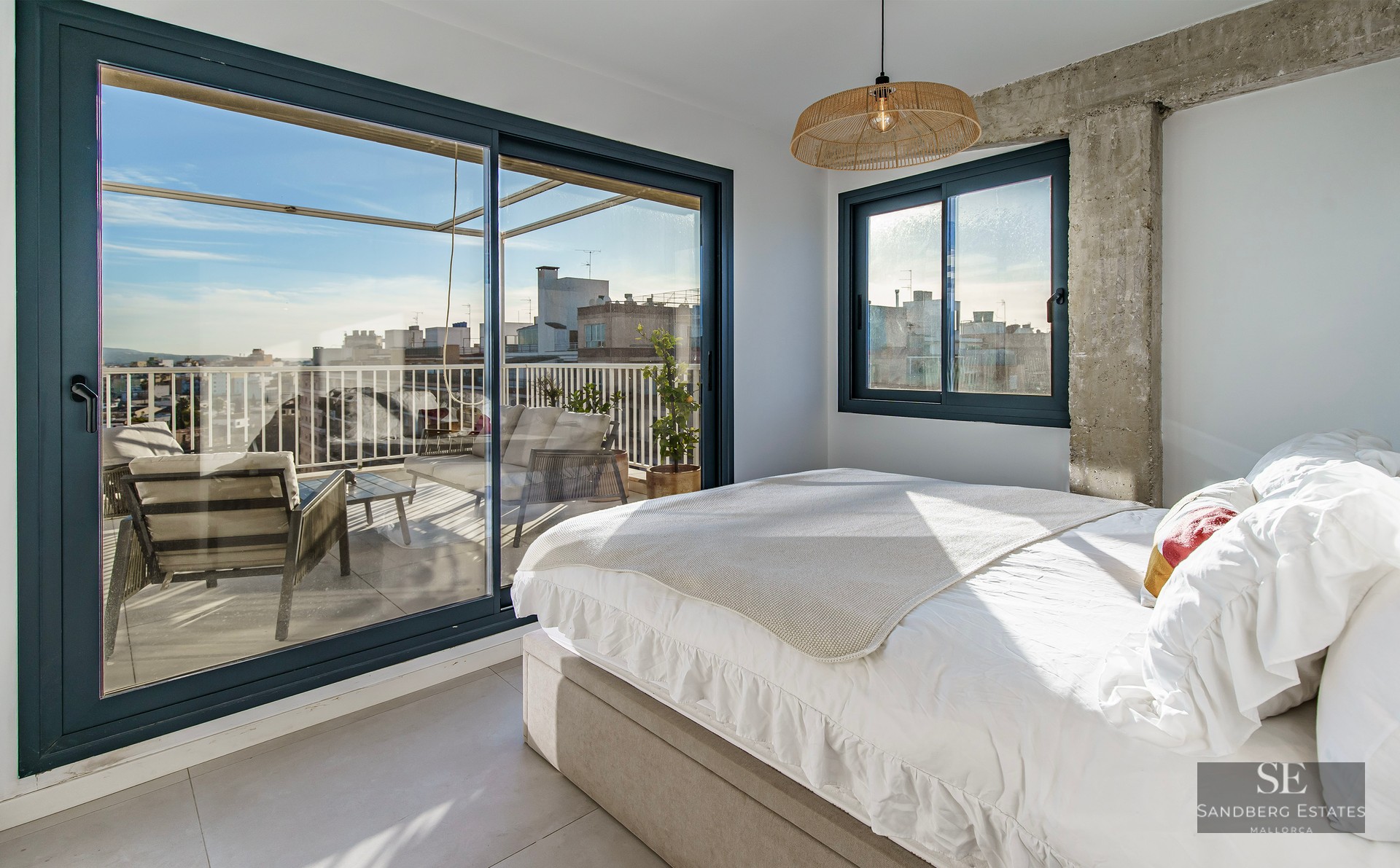 Bright bedroom with white bedding and large sliding glass doors opening to a private terrace with city views.