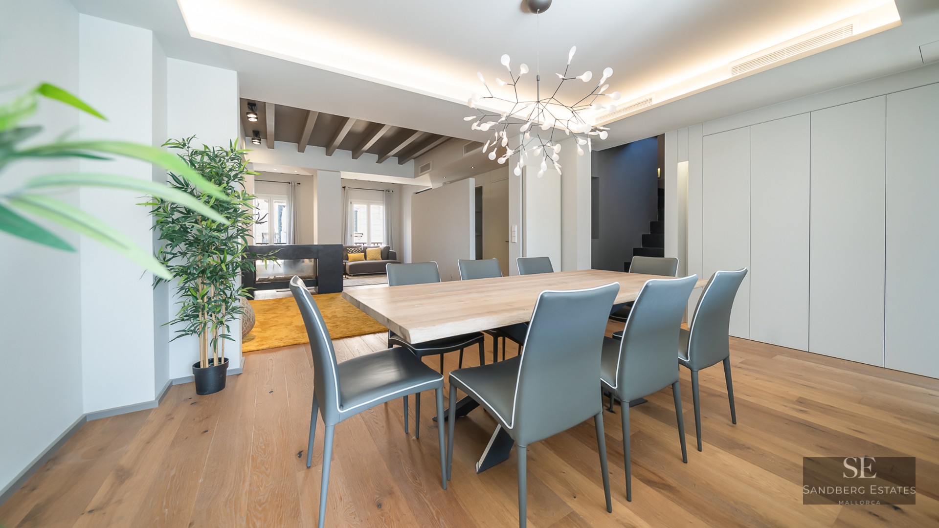 Spacious modern dining room featuring a large wooden table, grey chairs, and a branch-style designer chandelier.