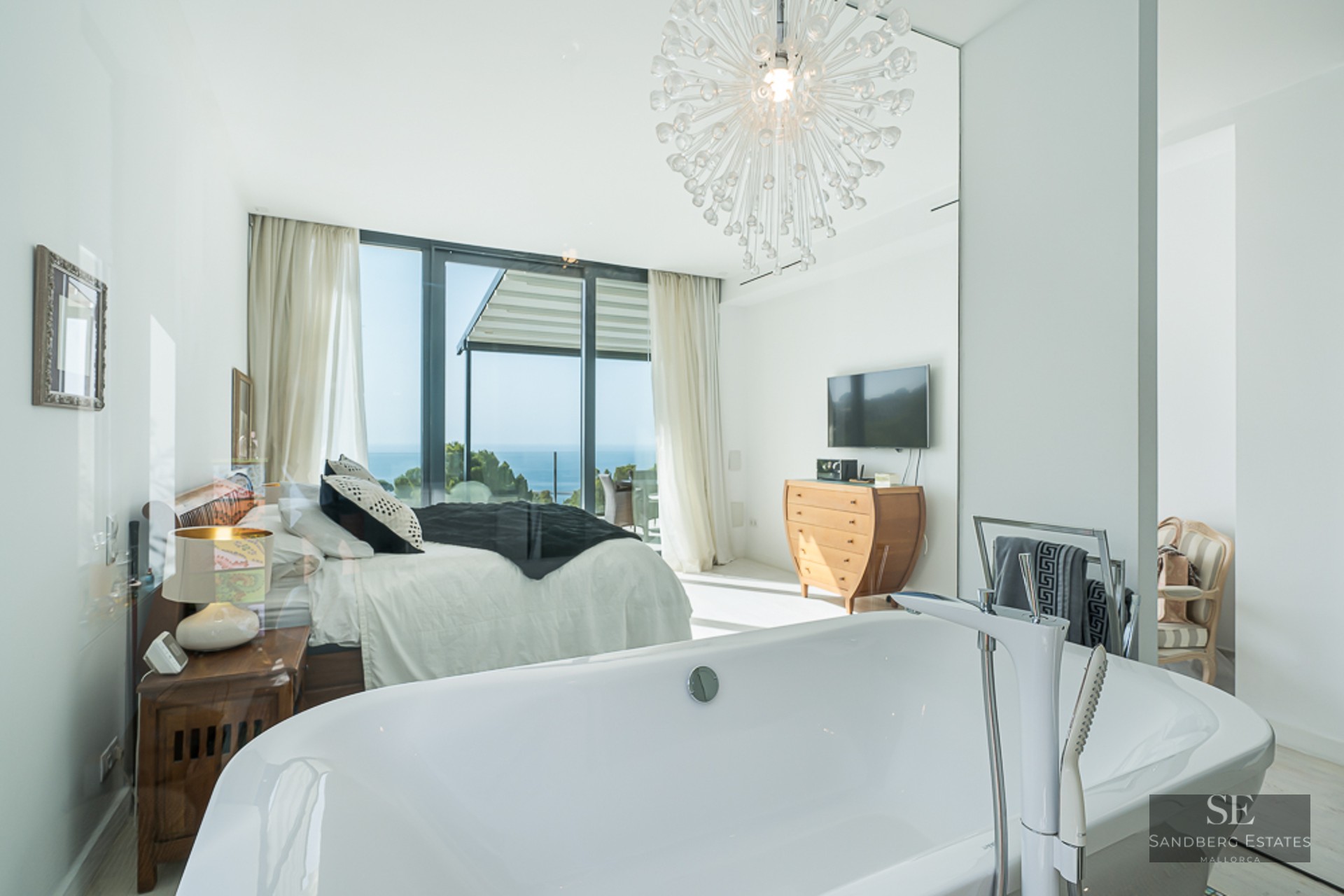 Modern master suite featuring a white freestanding bathtub in the foreground and a large bed with a sea view.