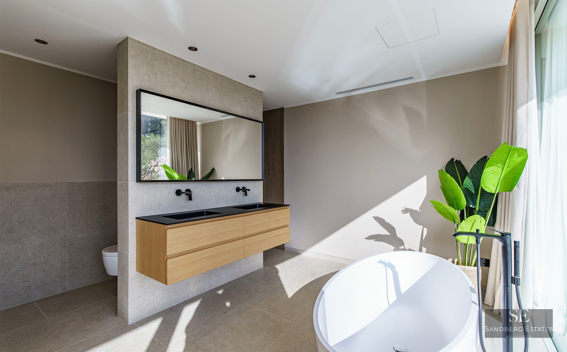Spacious master bathroom featuring a white freestanding tub, floating wooden double vanity, and matte black fixtures.