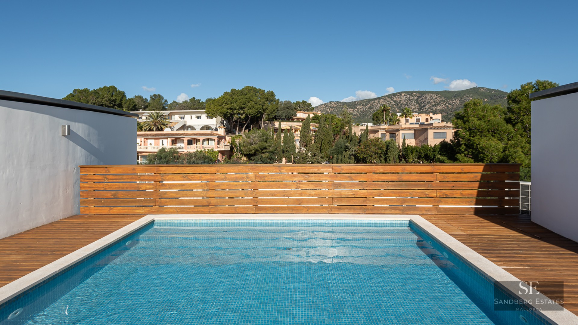 Une piscine rectangulaire sur le toit avec des carreaux bleus et une terrasse en bois, surplombant des collines vertes.