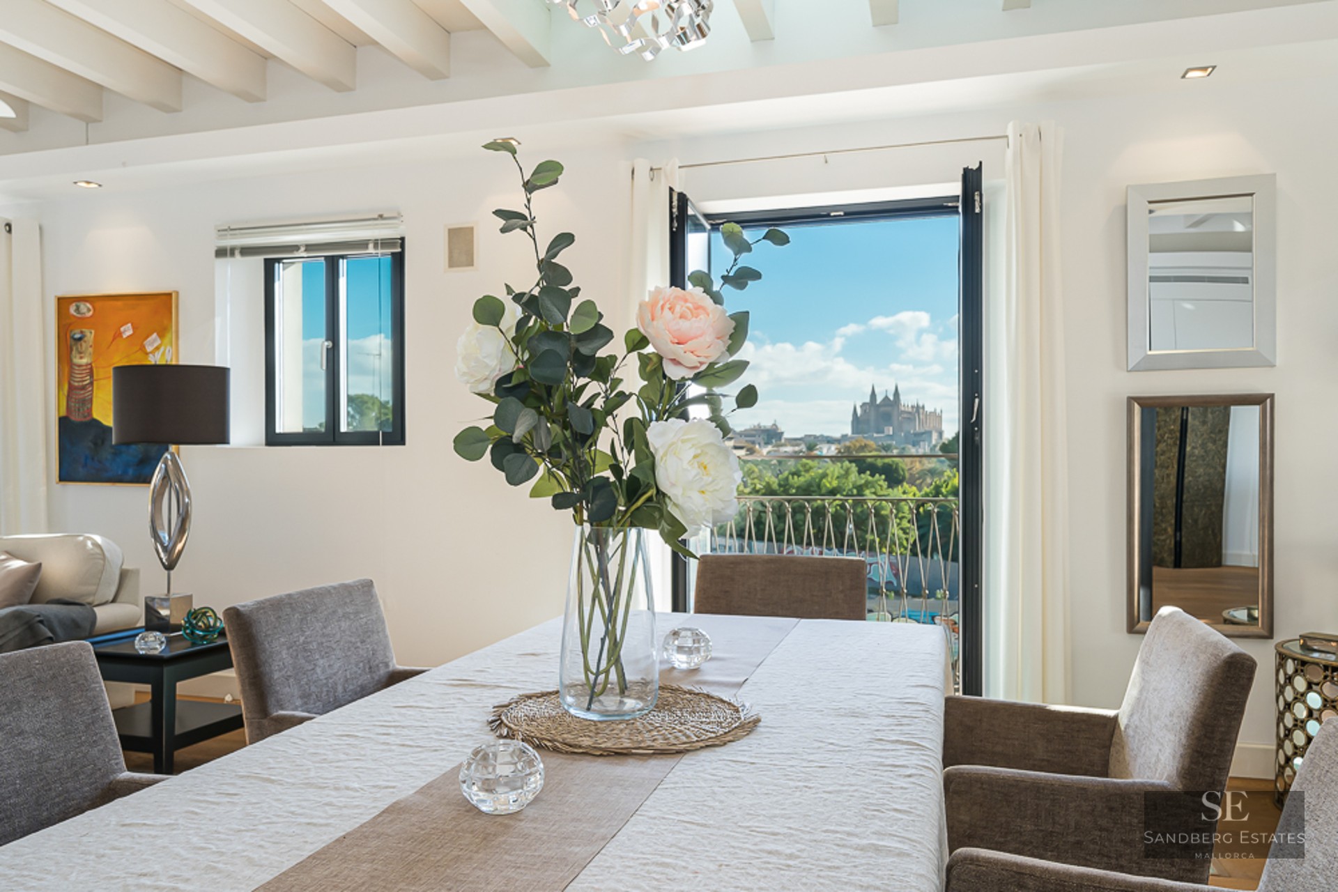 Bright dining room with white table, grey chairs, and a view of Palma Cathedral through a balcony door.