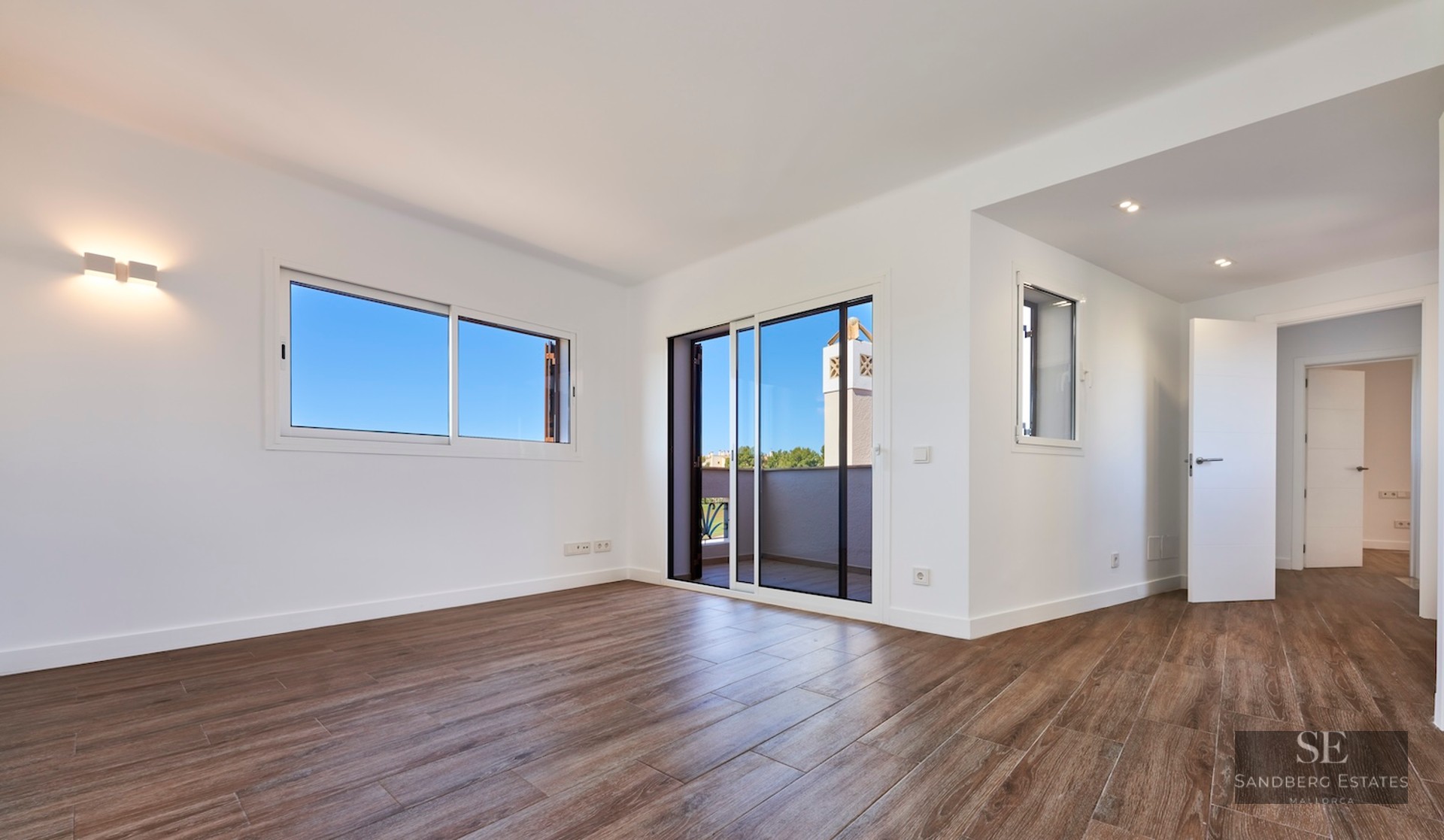 Empty room with white walls, wood-effect tile floors, and a sliding glass door leading to a terrace.