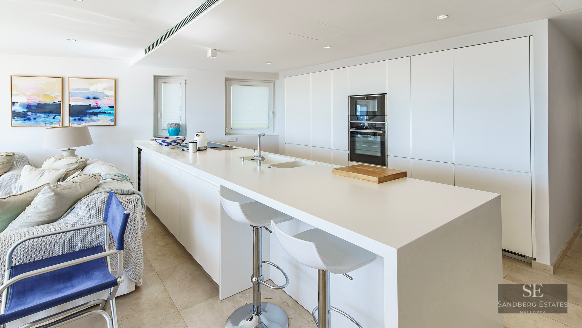 A bright, modern white kitchen featuring a large central island with bar stools and integrated appliances.
