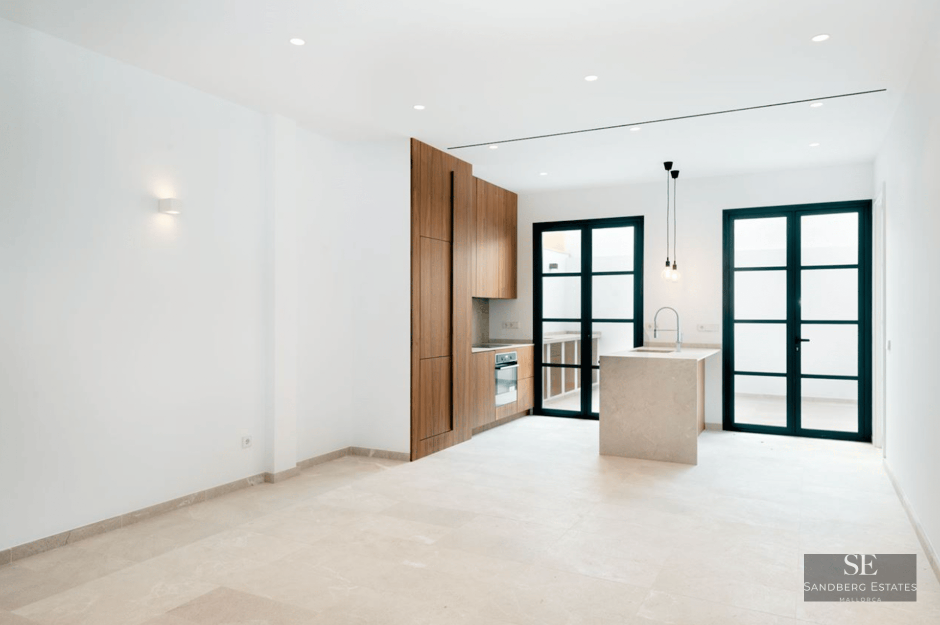 Modern kitchen with wood cabinets, stone island, and large black-framed glass doors leading to a terrace.