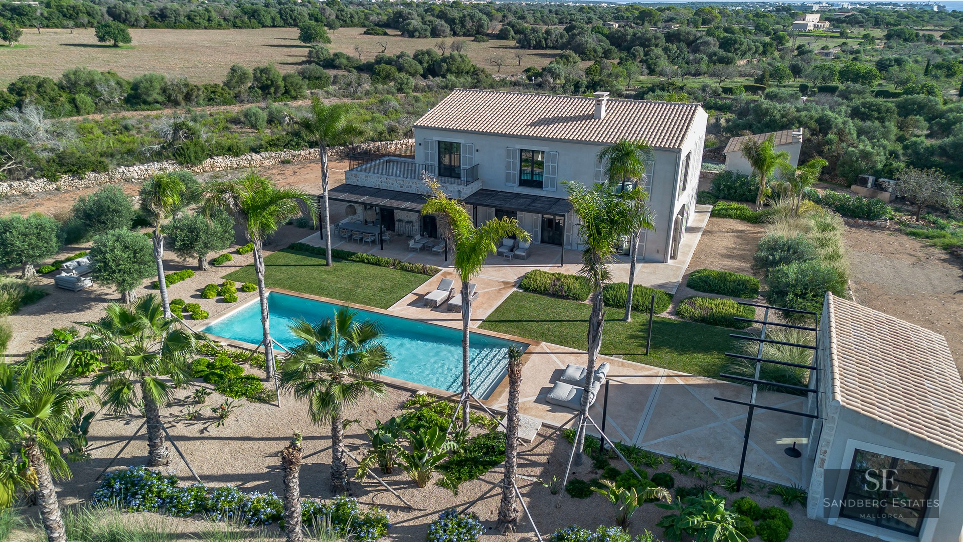 Aerial view of a luxury villa with a turquoise swimming pool, palm trees, and landscaped gardens.