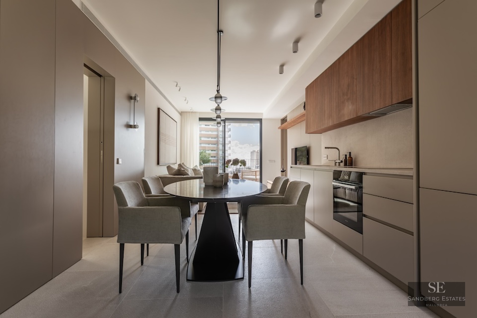 Contemporary dining room featuring a black oval table, grey upholstered armchairs, and a sleek minimalist kitchen.