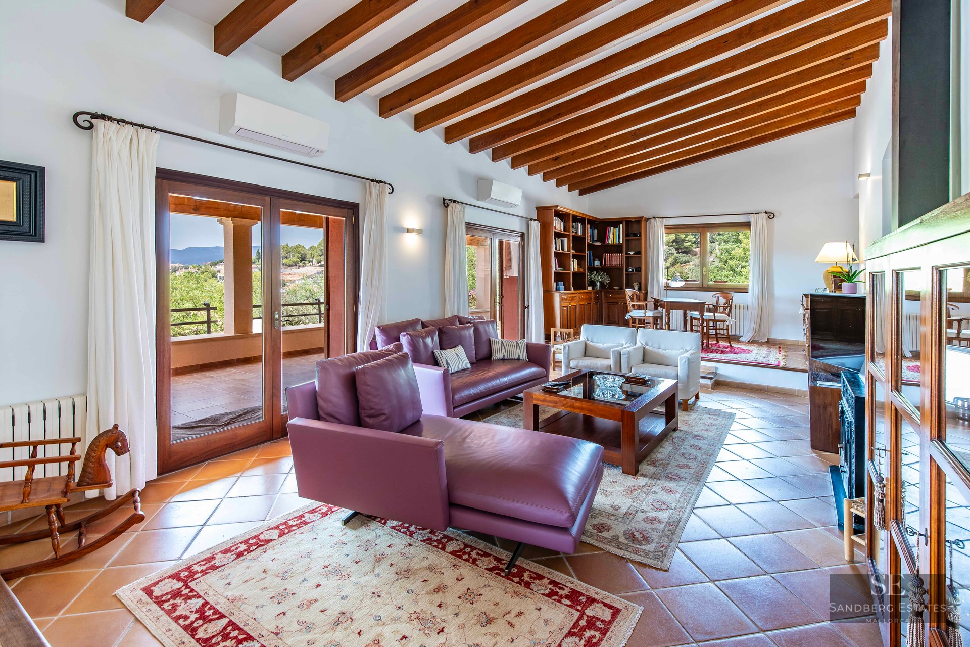 Bright living room with purple leather sofas, wooden ceiling beams, terracotta tiles, and terrace views.