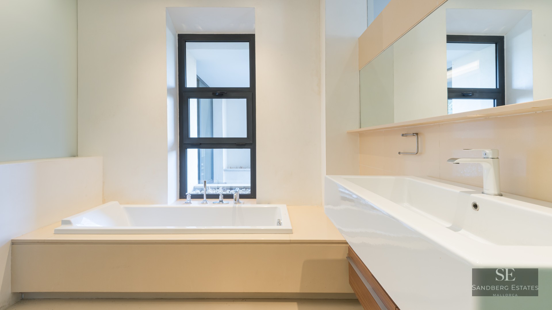Modern bathroom featuring a built-in white bathtub next to a window and a large white rectangular sink with a wide mirror.