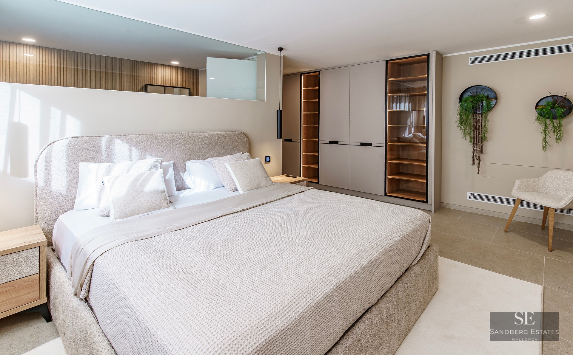 Modern master bedroom with large upholstered bed, integrated wooden wardrobes with LED lighting, and neutral decor.