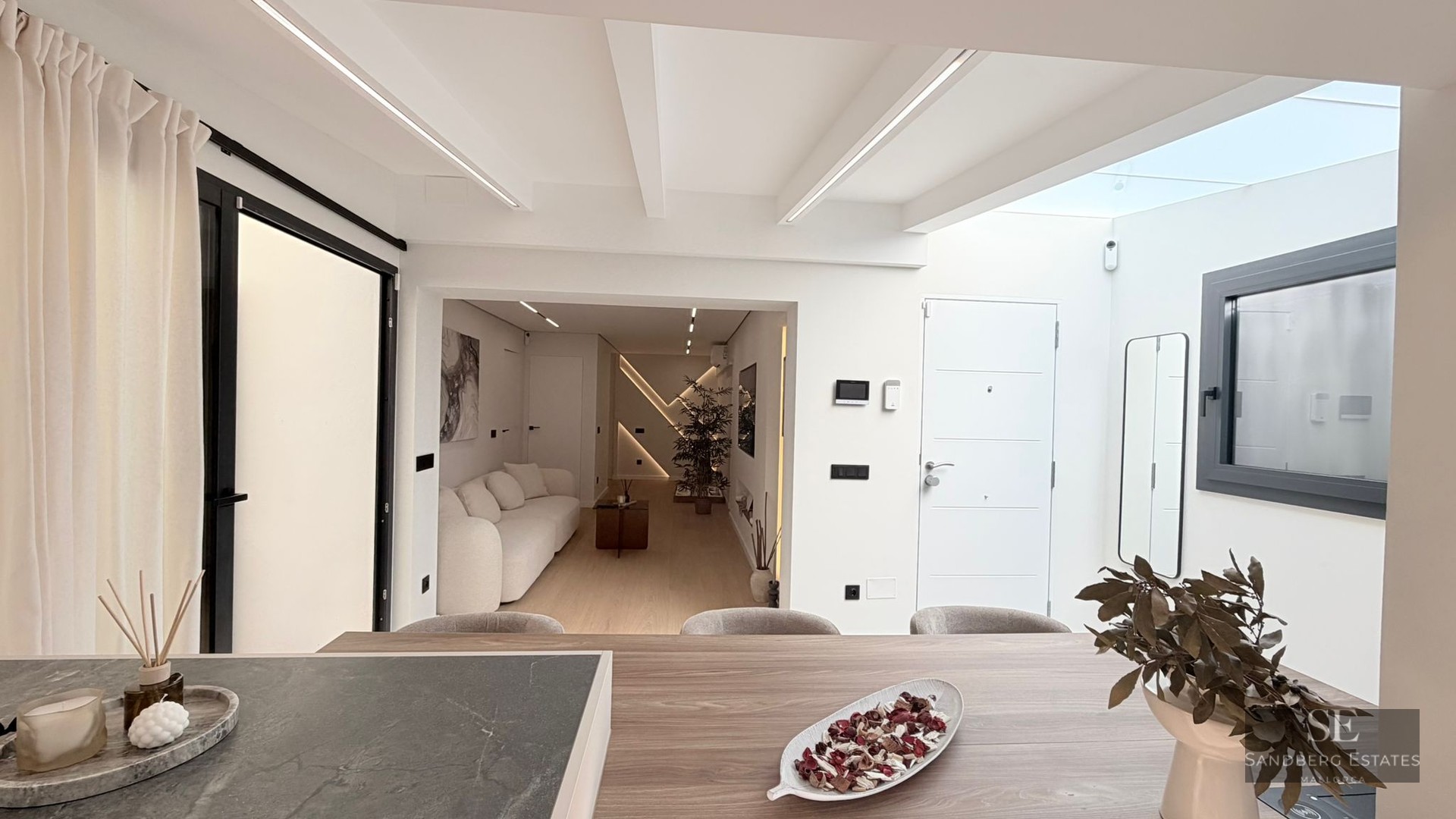 Bright modern interior featuring a white sofa, wood textures, and a skylight illuminating the living and entrance area.