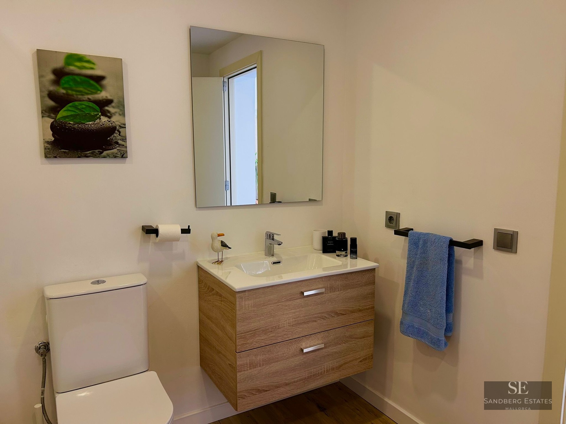 A modern bathroom featuring a floating wood vanity, white toilet, and minimalist decor.