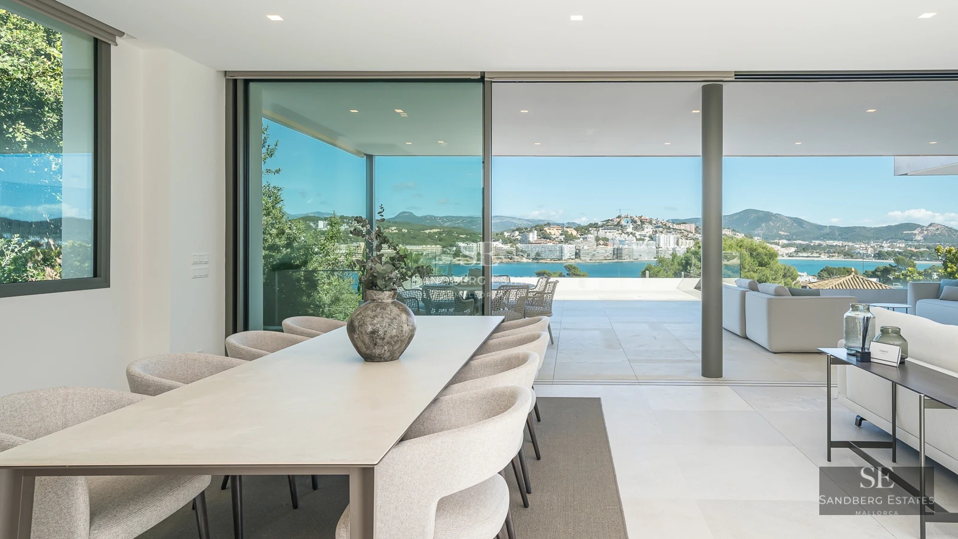 Spacious, bright living room with panoramic windows, light wood flooring and modern furniture. Overlooking garden and pool. Elegant and minimalist design.