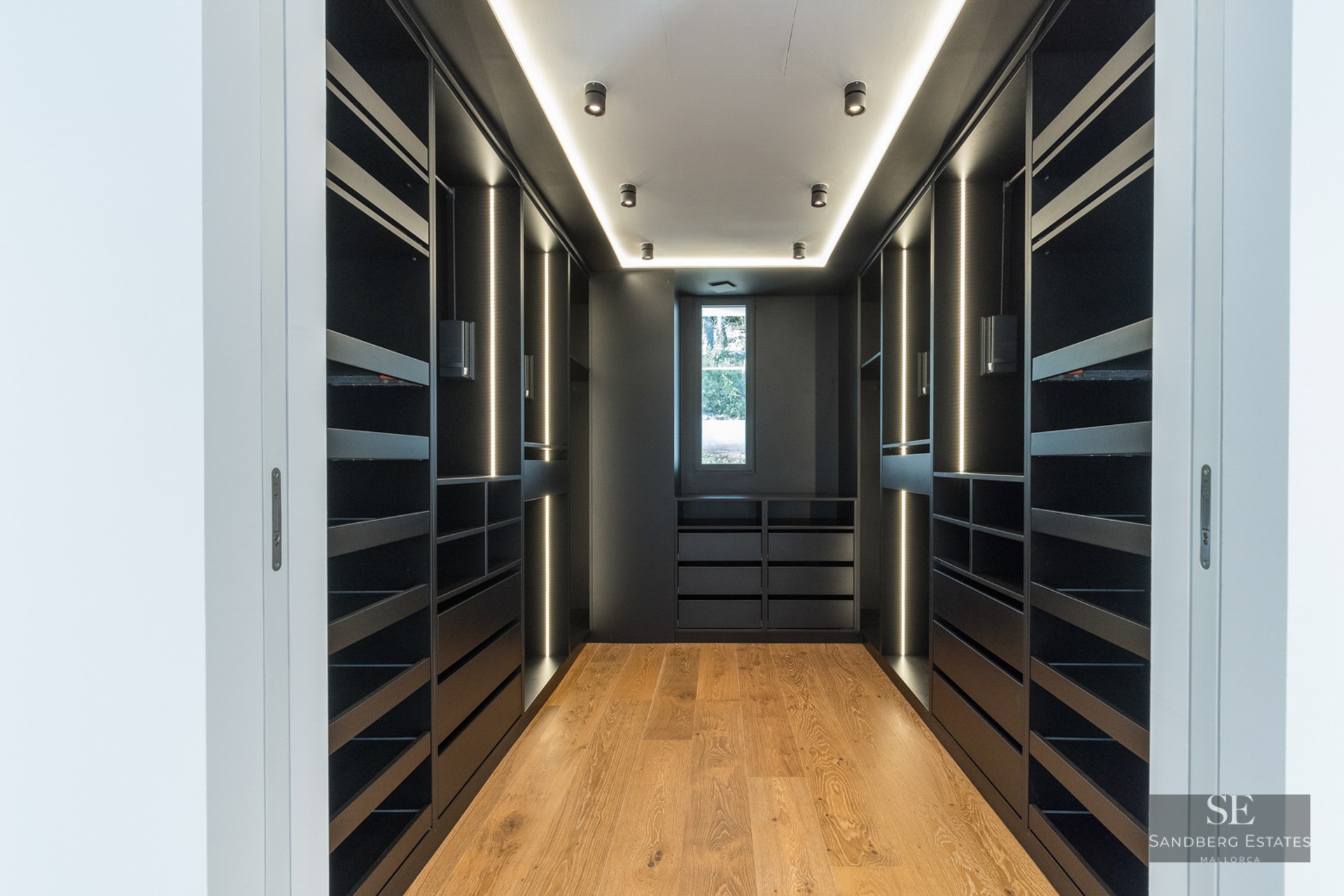 Sleek black walk-in closet with integrated LED lighting and light wood floors.