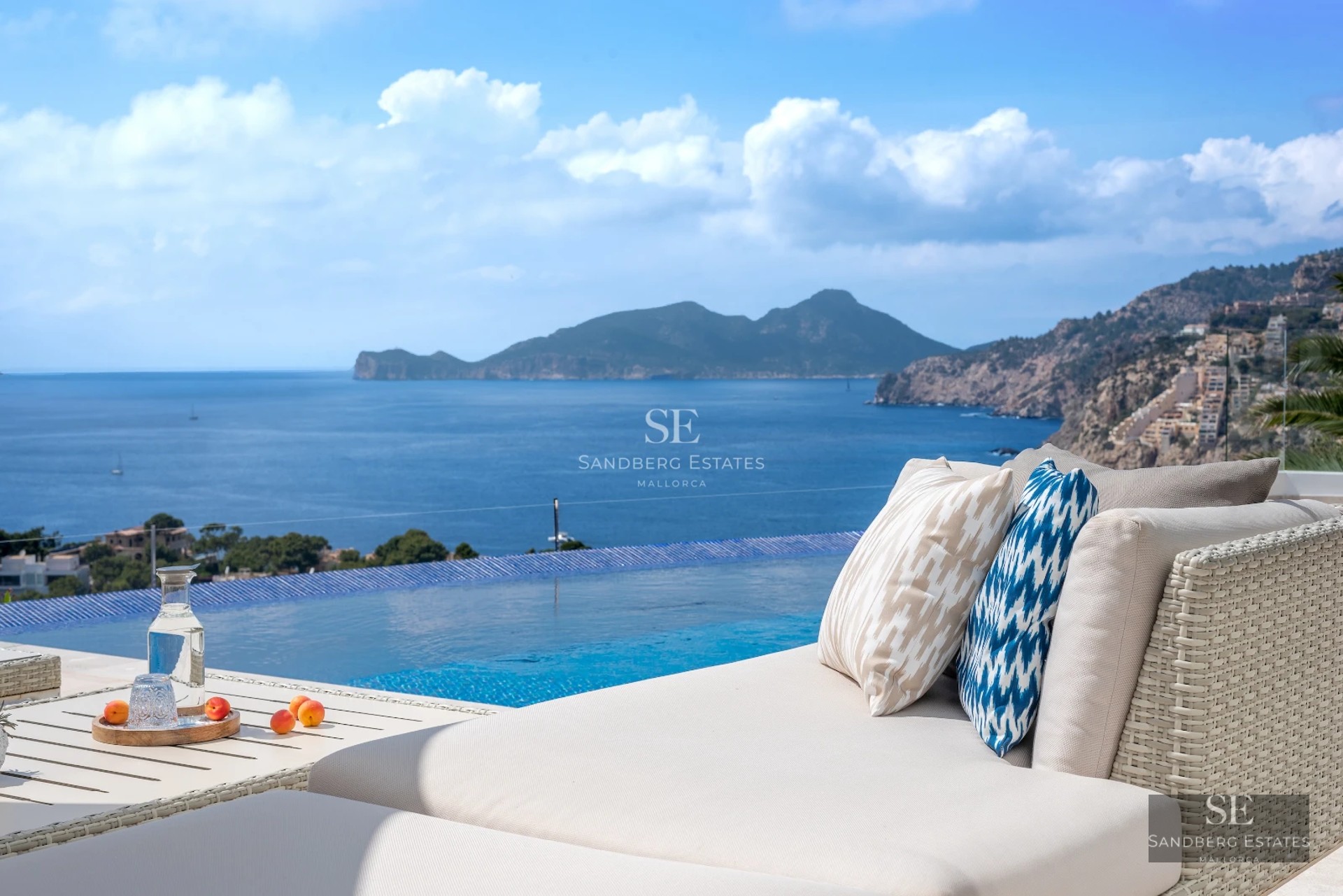 Spacious balcony with light wood flooring, glass railing, sea view, and modern outdoor furniture. Abundant natural lighting.