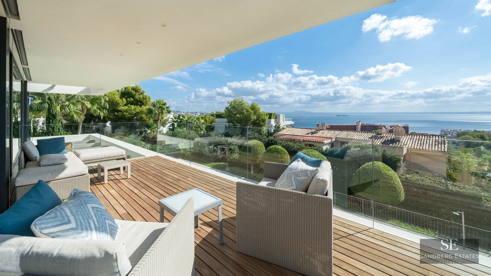 Modern terrace with wooden decking, white sofas, and glass railing featuring panoramic sea views.