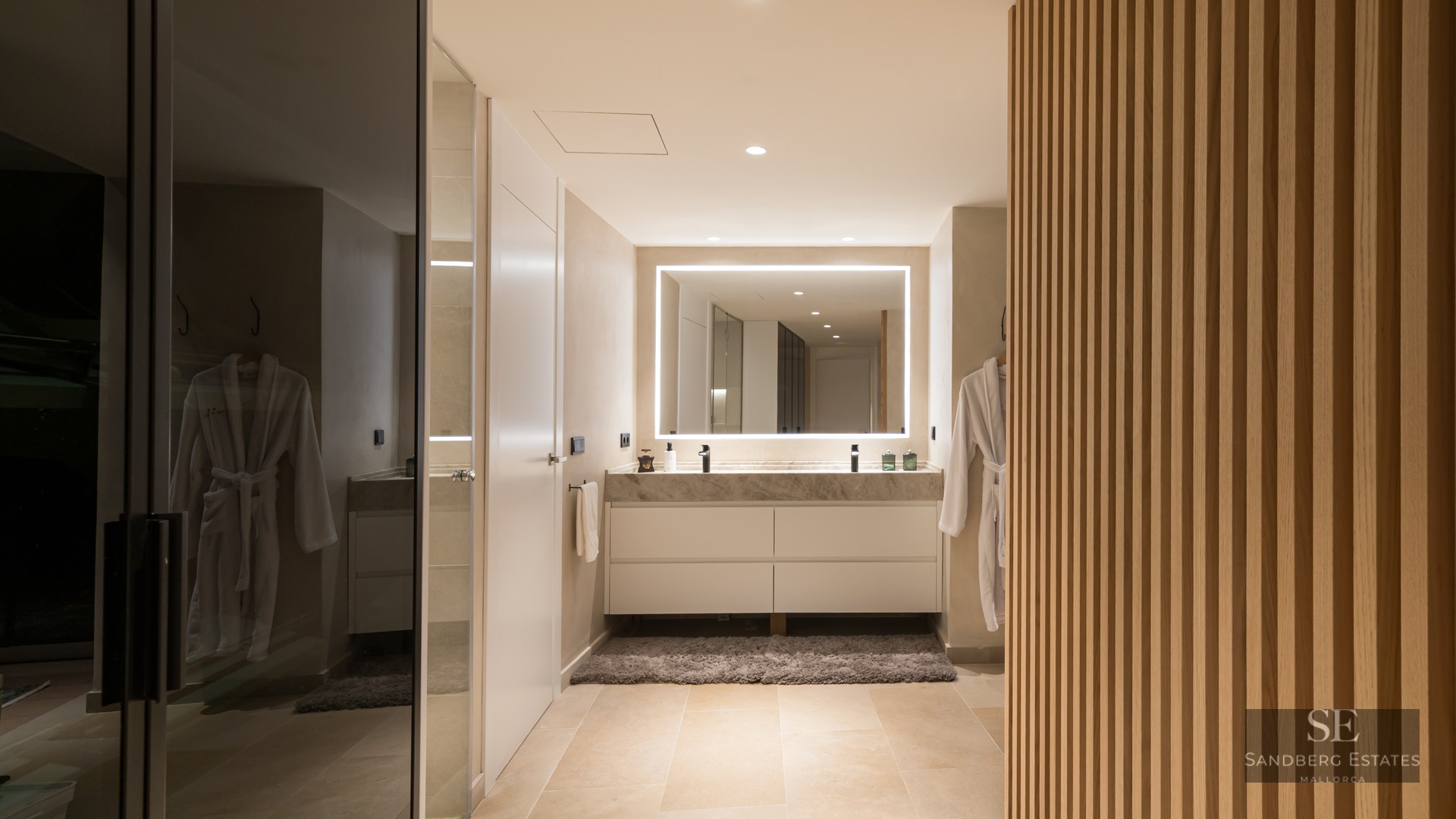Modern bathroom featuring a marble double vanity, large backlit LED mirror, and vertical wood slat wall.